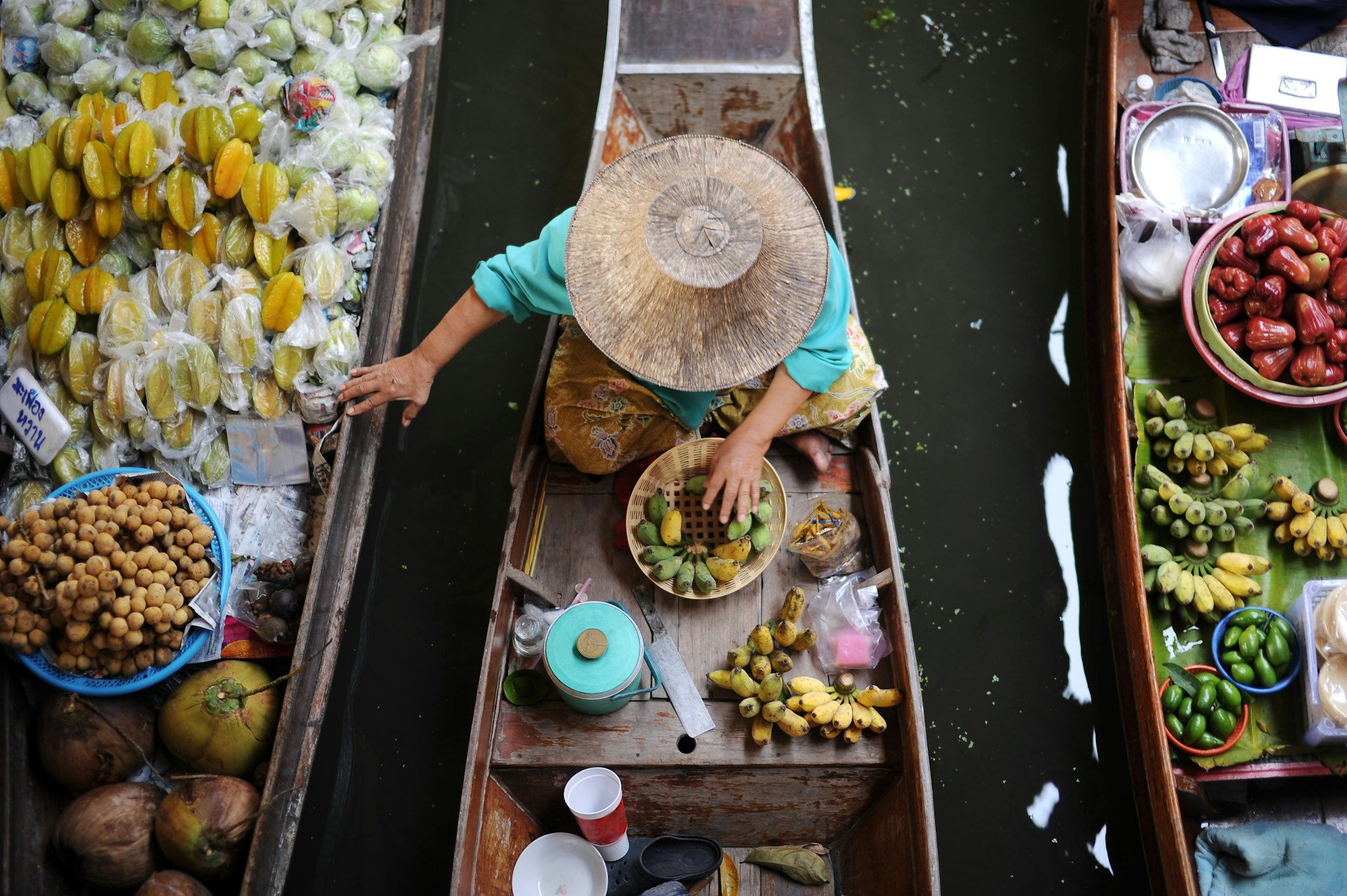An aerial shot of a Thai woman on a boat looking at rice and other produce at Damnoen Saduak Floating Market in Thailand