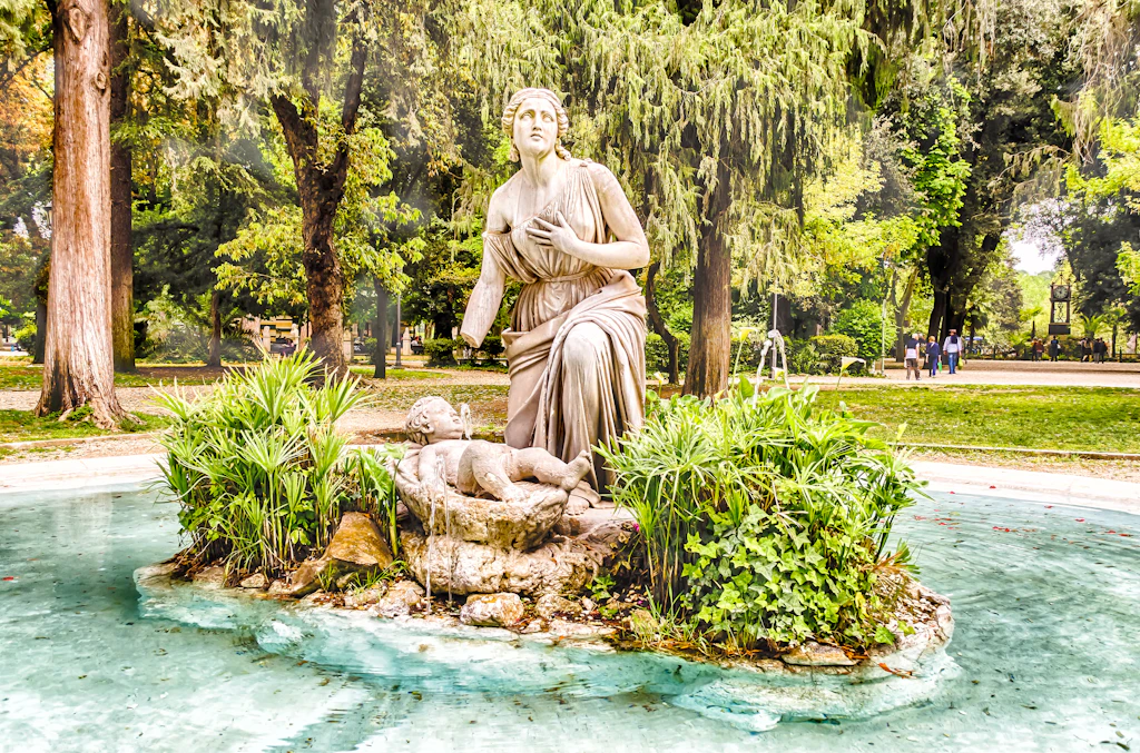 A statue is the centerpeice of a fountain in parkland