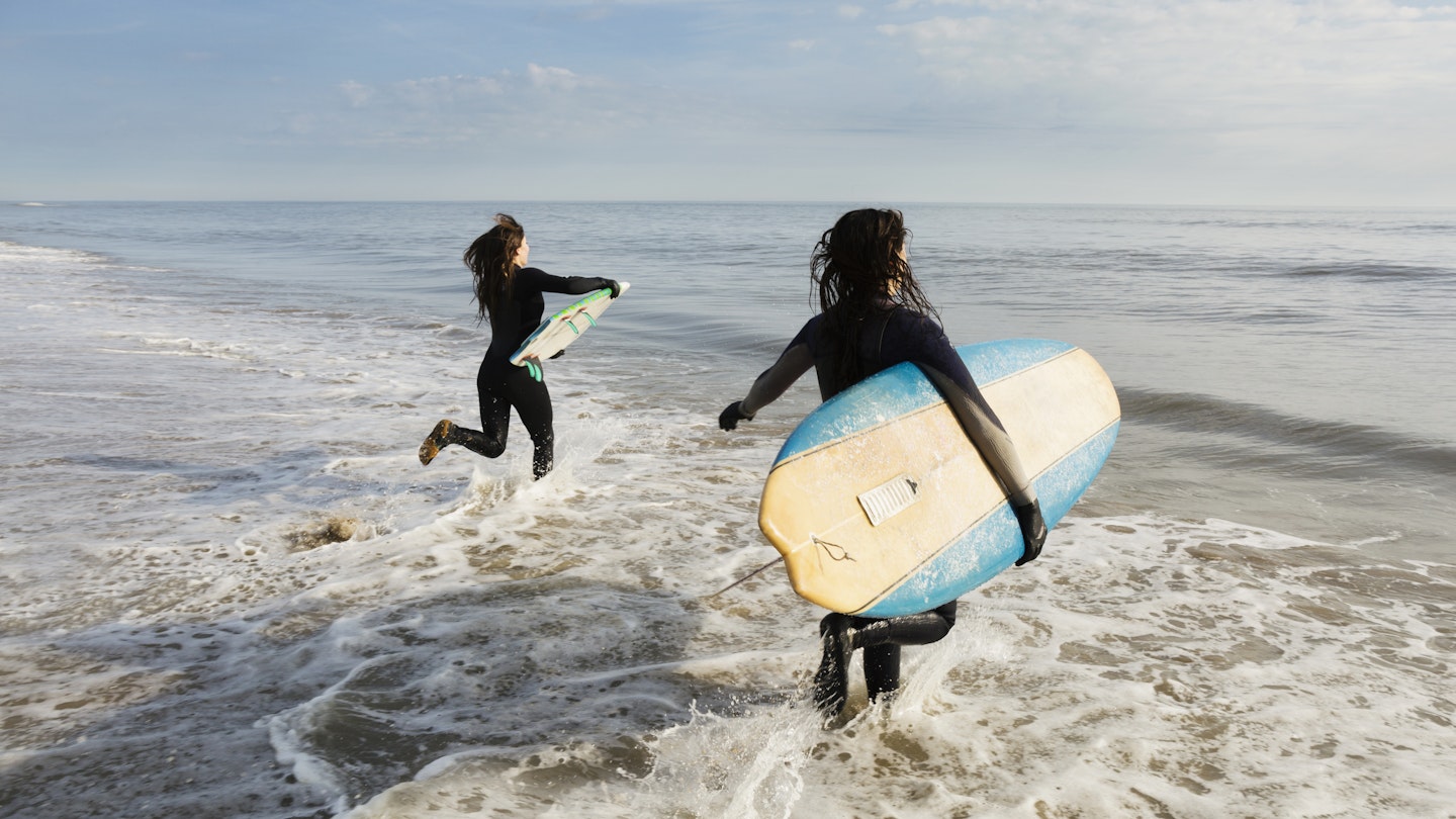 Surfers carrying boards in waves