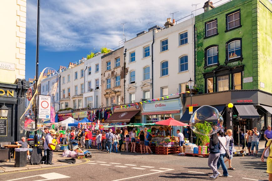 A row of pastel-colored houses on a street lined with shops and busy with people