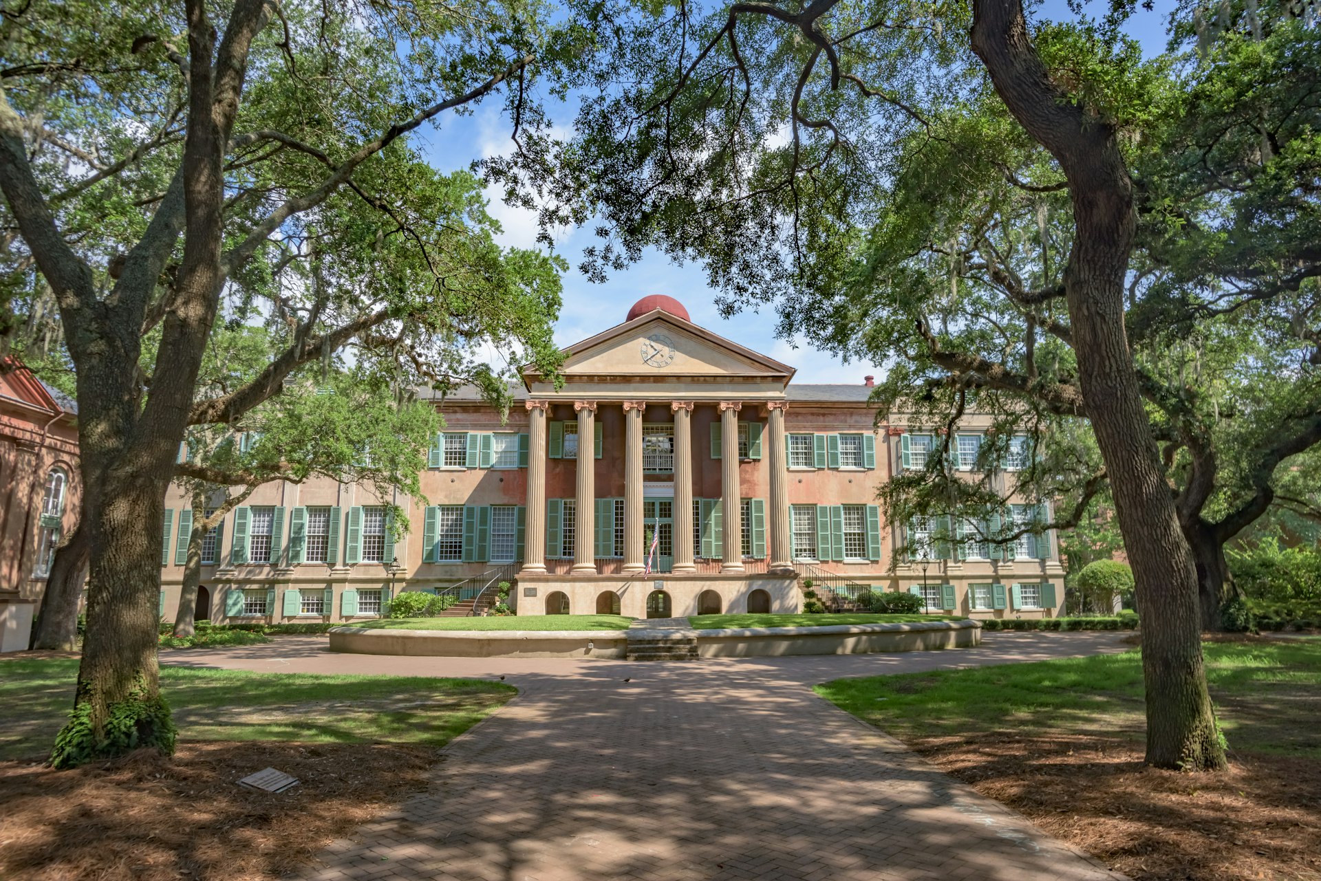 Randolph Hall, the main academic building on the College of Charleston campus, sits behind the shade of trees on the lawn.