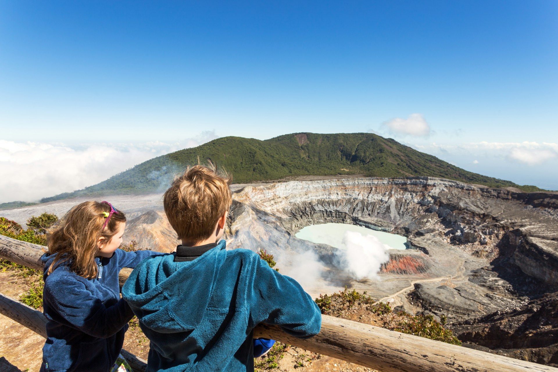 Two children gaze down into a crater at an active volcano