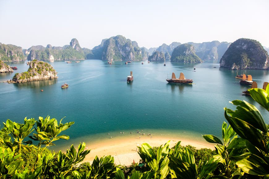 A view of Halong Bay from a high vantage point on an island. The bay is made up of many limestone islets, jutting out from the calm blue waters.