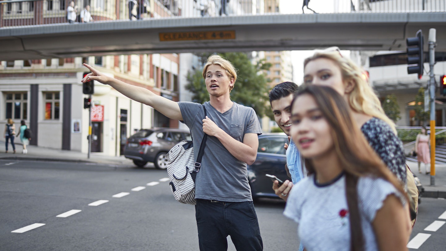 Young man hailing taxi while standing with friends on a Sydney street.