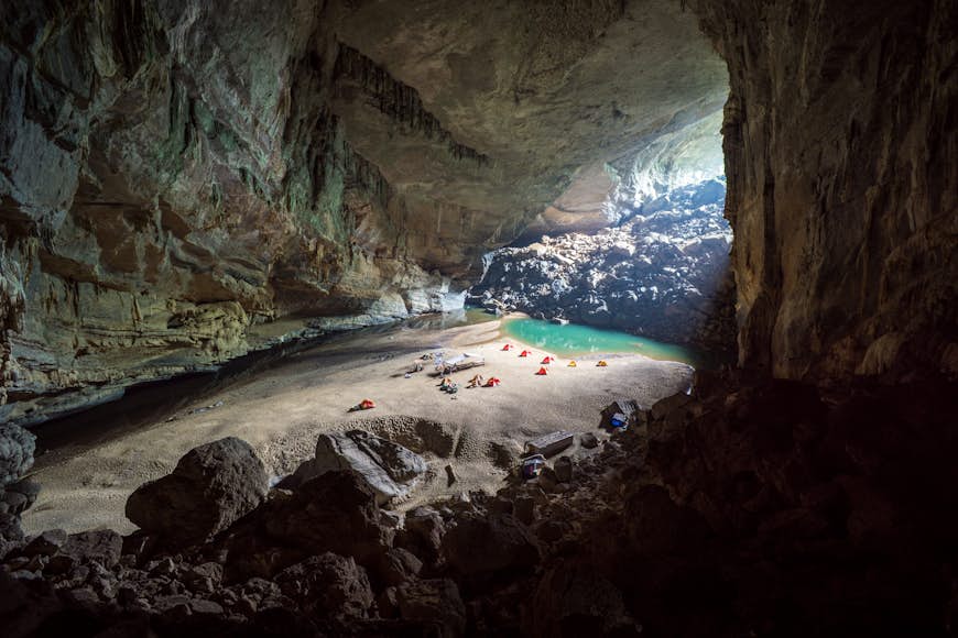 A handful of yellow and red tents can be seen ereceted on a sand bar near the entrance to the cavernous Hang En Cave in Vietnam. The cave is one of the biggest in the world, and the tents all look tiny in comparison to the vast space.