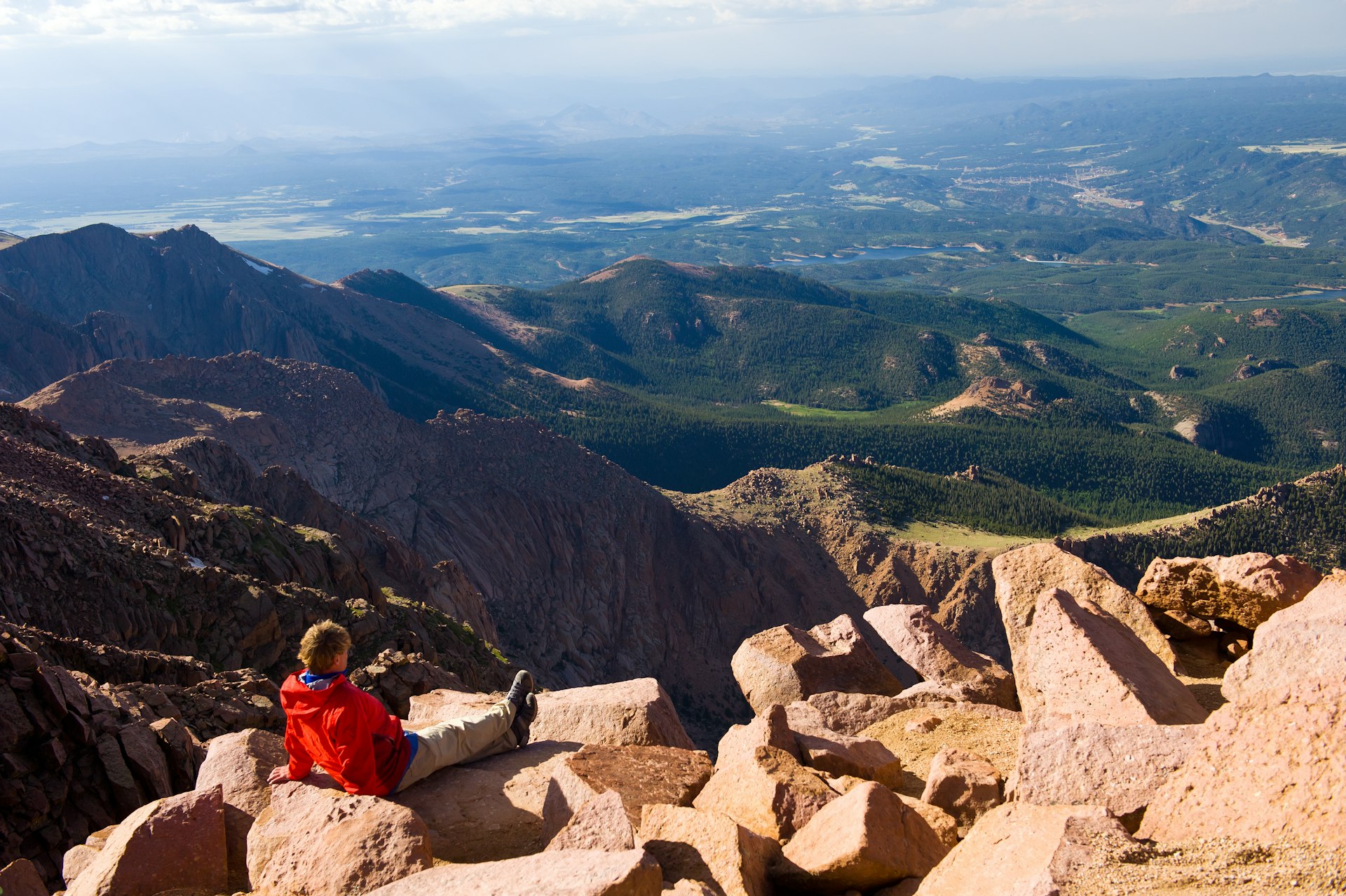 A young male hiker enjoying the scenic view from Pikes Peak on beautiful, sunny day, kicking back on warm sunny rocks with his legs outstretched in front.