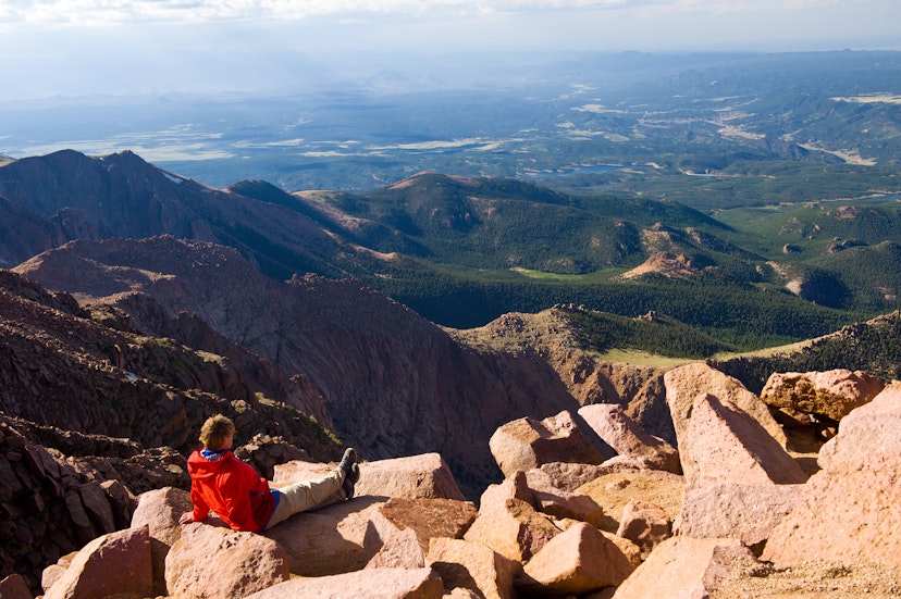 "Vista Scenic View from Pikes Peak Summit Colorado.  Hiker enjoying scenic view on beautiful, sunny day.  Young athletic man kicking back on warm sunny rocks.  Legs outstretched in front.  Captured as a 14-bit Raw file. Edited in ProPhoto RGB color space."