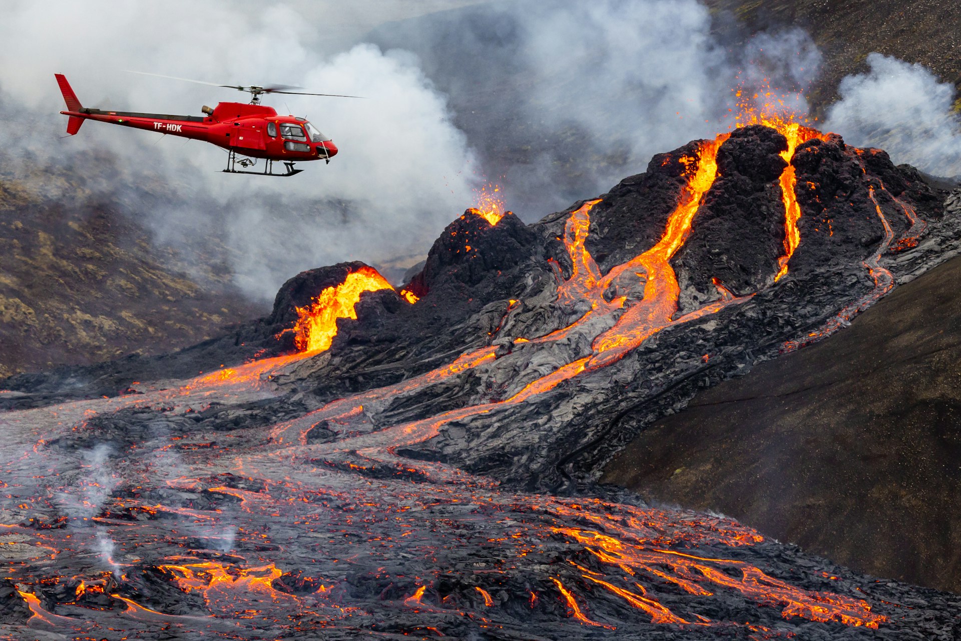 A helicoptor flies in front of lava flow from an active volcano