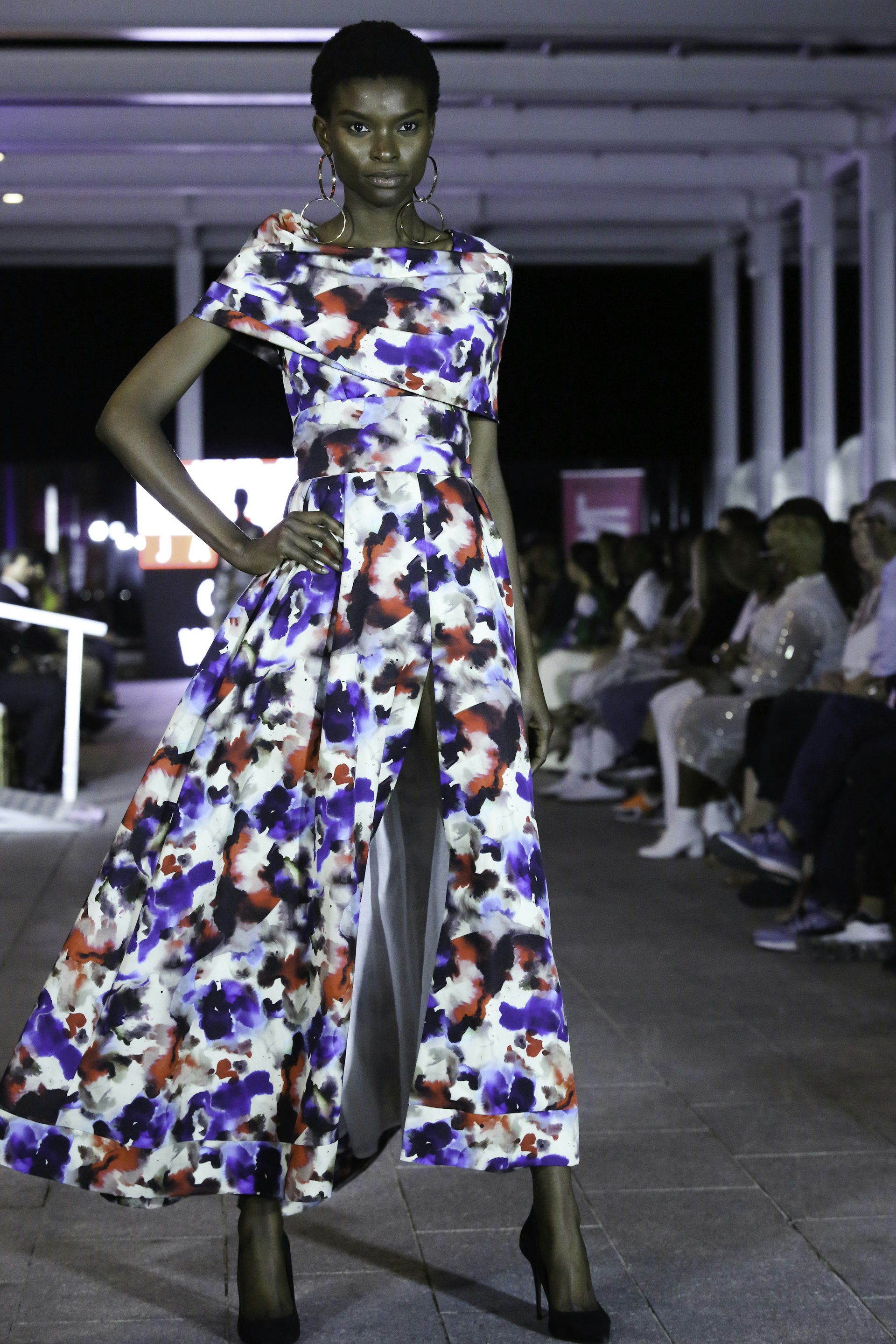 A model walks down a catwalk wearing a colorful dress with black high heels at Jamaica's Fashion Week.
