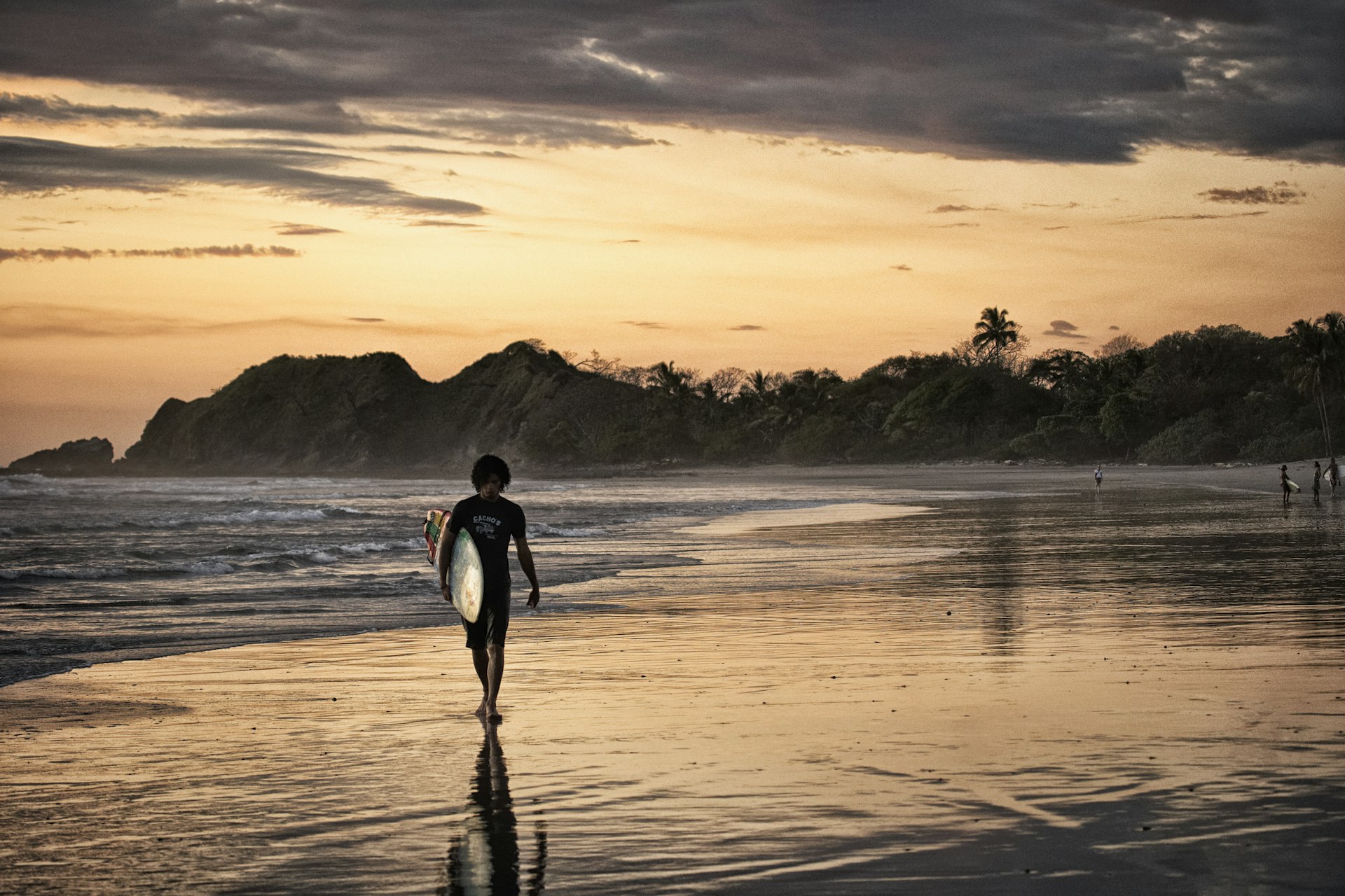 A surfer holding his board is silhouetted in the pink sunset light on Nosara Beach, Costa Rica