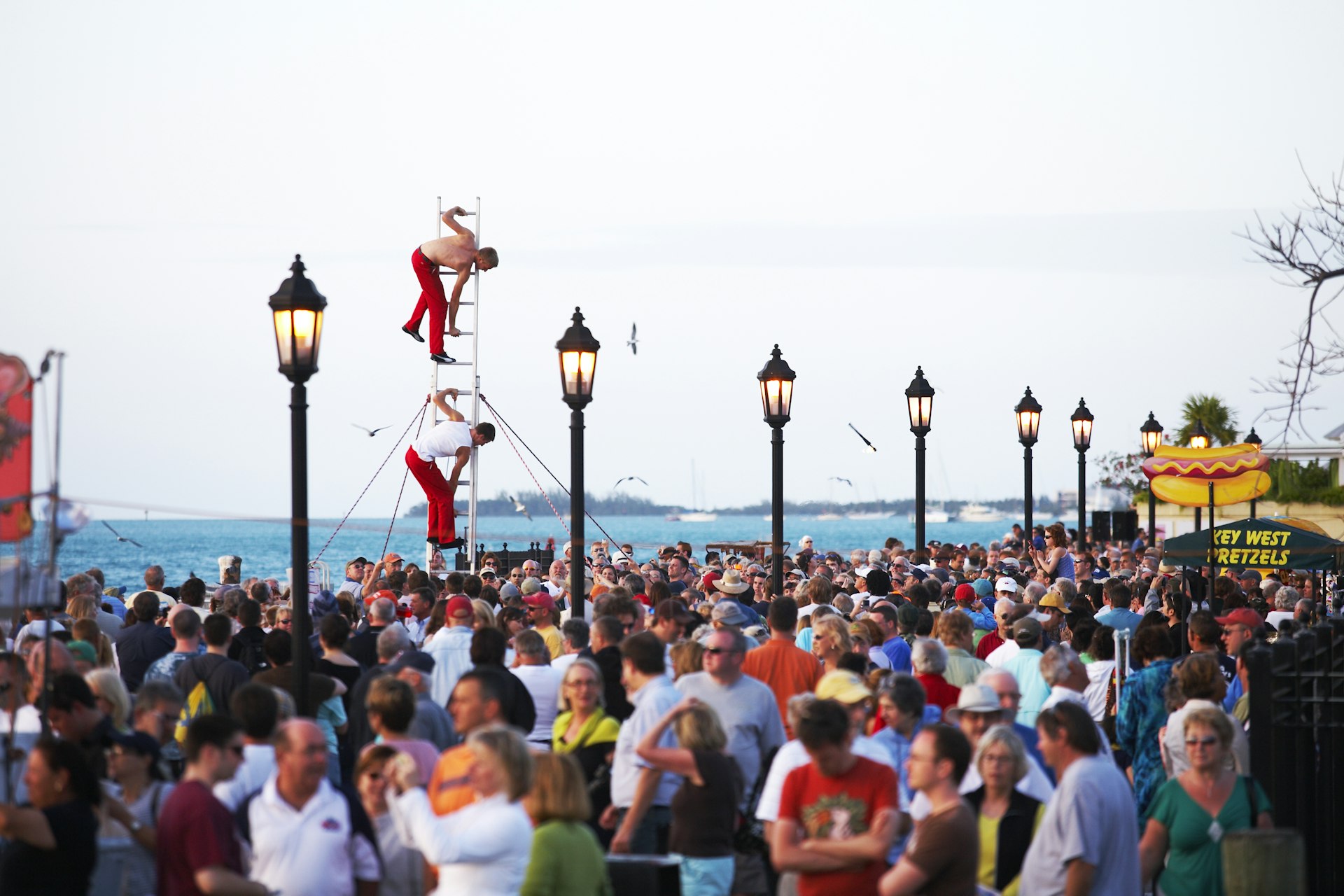 A crowd on an ocean promenade with street performers balanced on a ladder