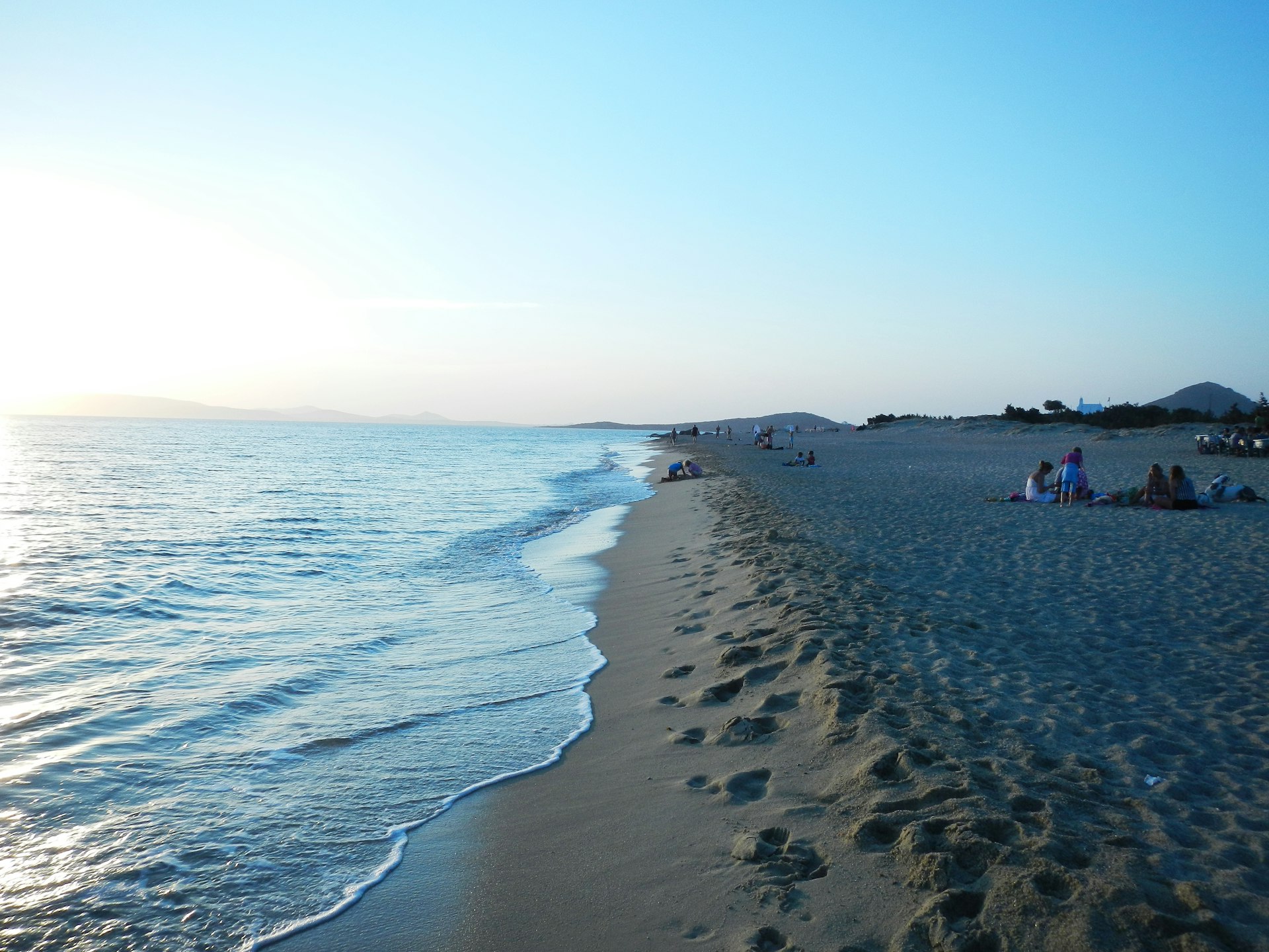 A view of gentle waves lapping a sandy beach at dusk on the island of Naxos, Greece.