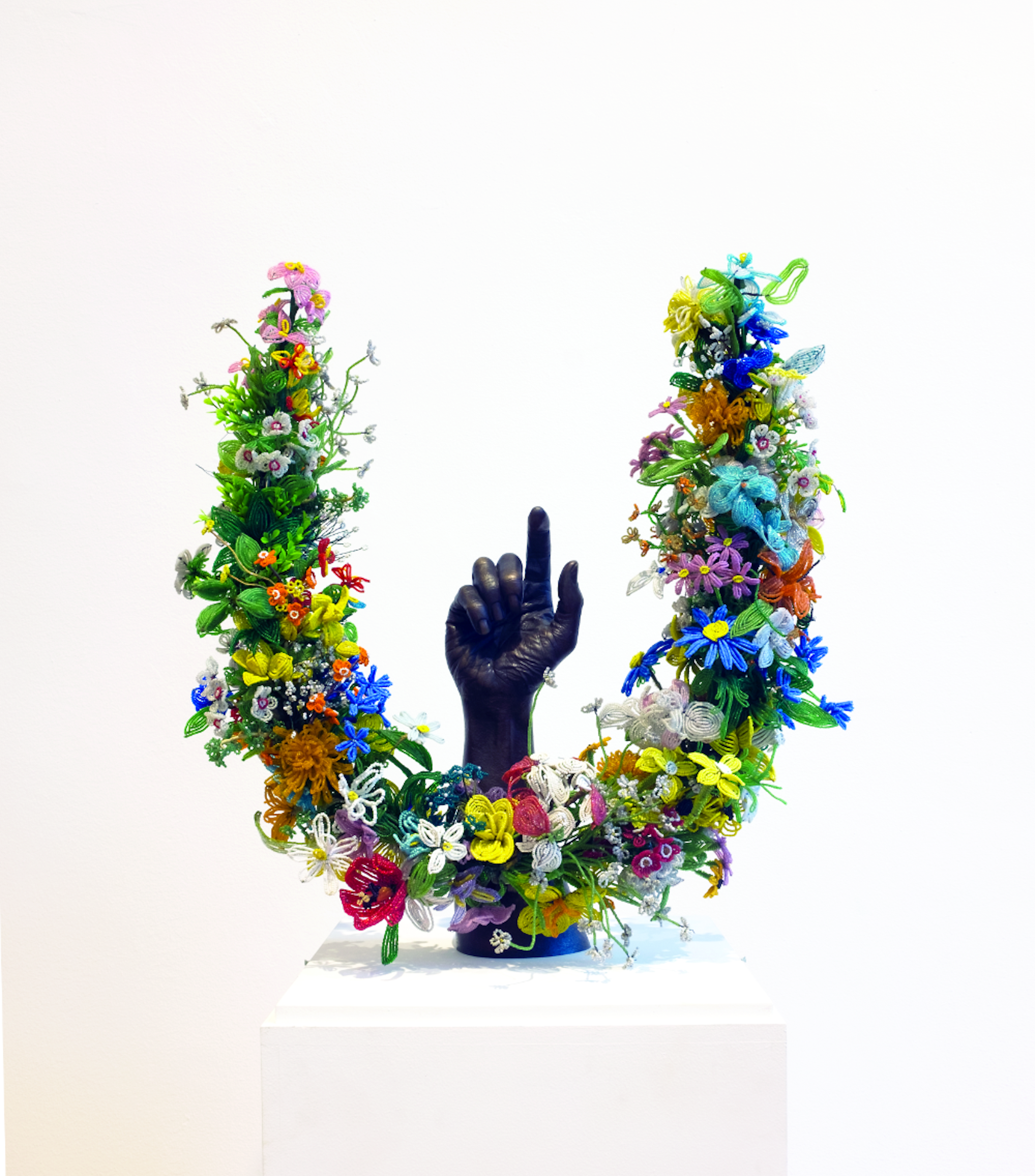 A sculpture of a black arm surrounded by flowers by Nick Cave