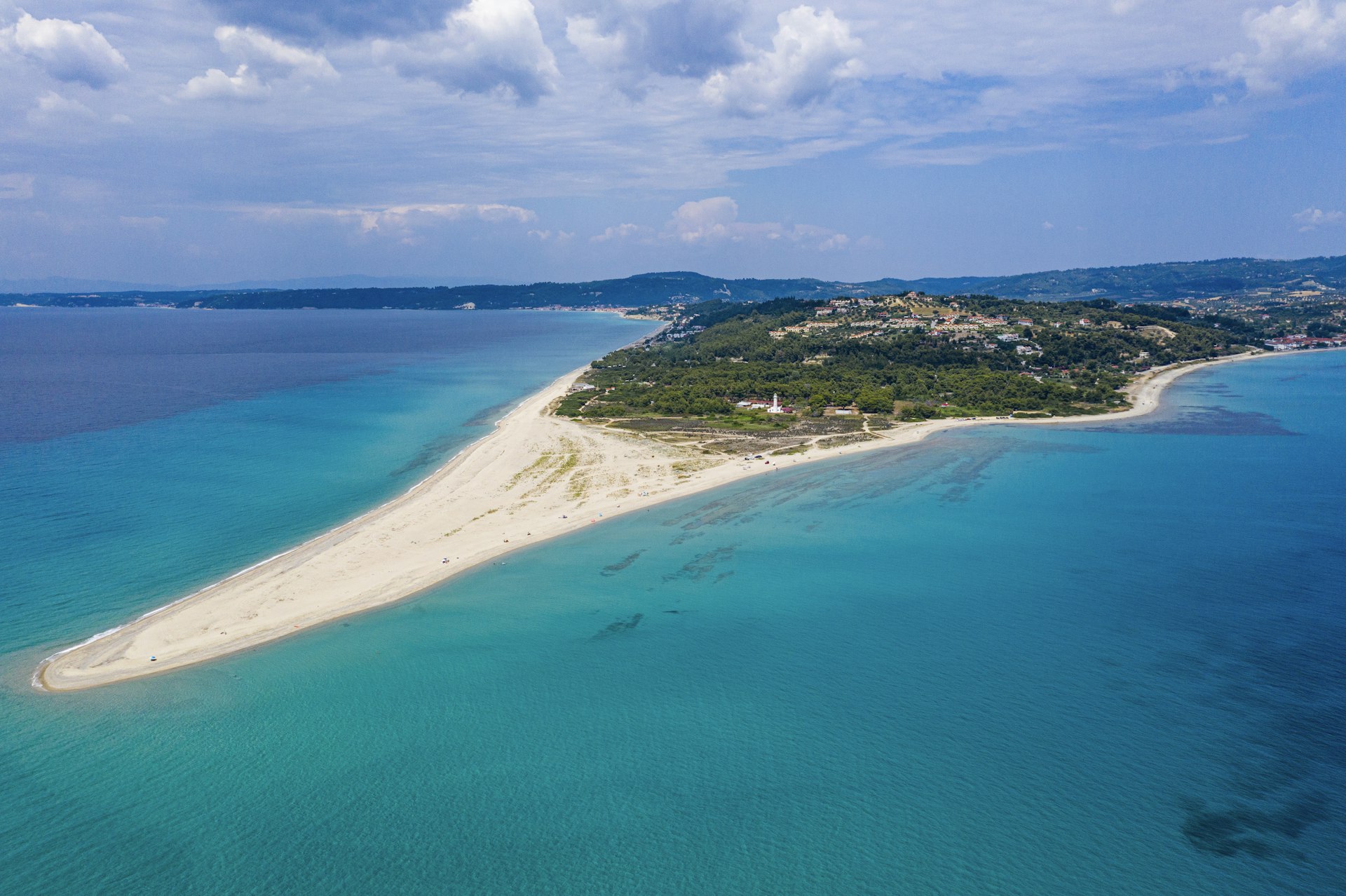 An aerial view of Possidi Beach in summer. The beach is uniquely triangular in shape, protruding from a forested island.
