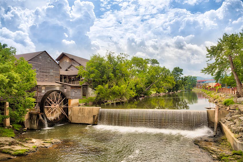 Landscape photo of a river and old mill with blue sky with clouds and the trees reflecting in the water.