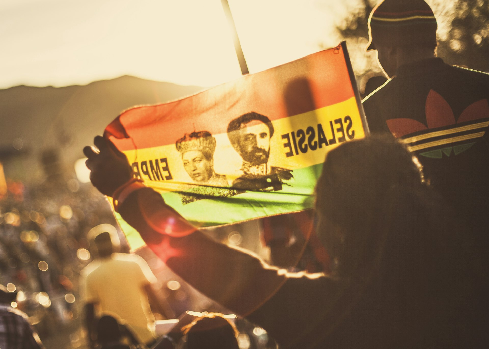A woman waves a flag with a picture of Haile Selassie against sunrise while watching Capleton perform at the Rebel Salute Festival 