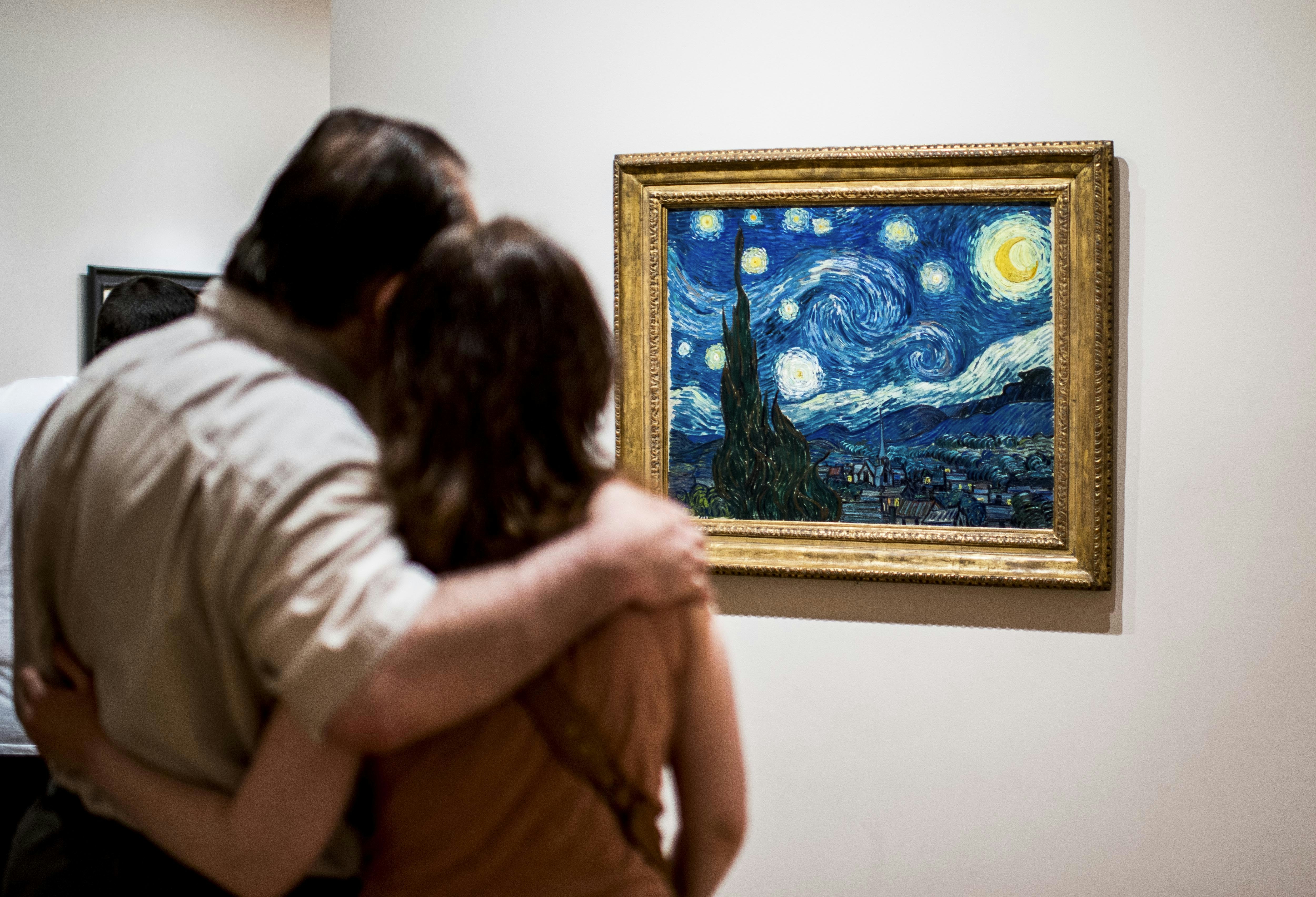 Two tourists, one with their arm around the other, look at The Starry Night by painter Van Gogh at Museum of Modern Art (MoMA), New York.