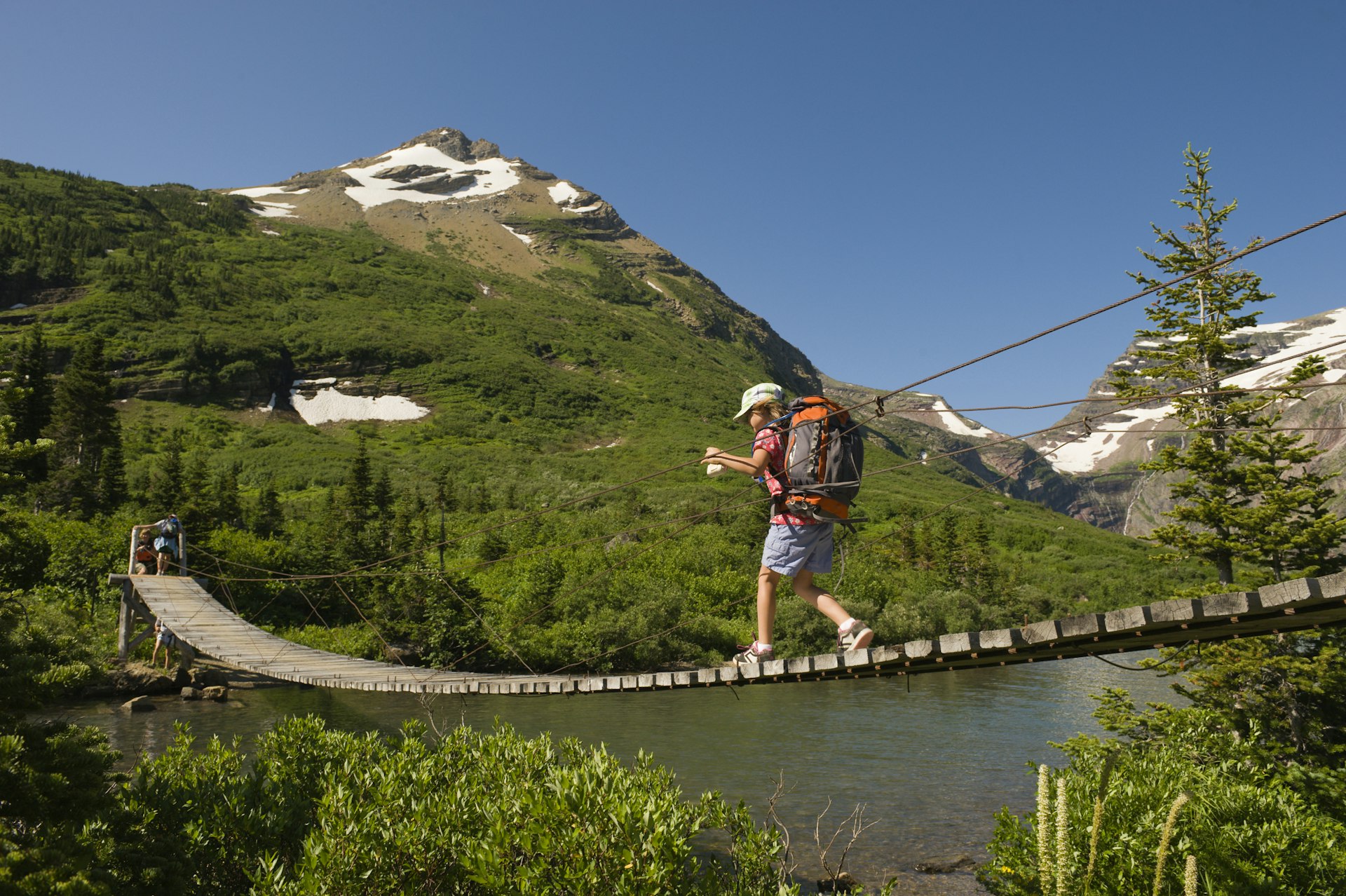 A young girl hikes over a suspension bridge in Glacier National Park, Montana.