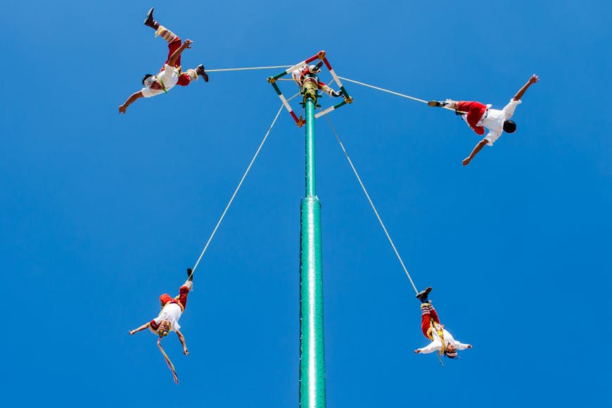 A group of men dressed in red suspended from a central pole - Voladores de Papantla