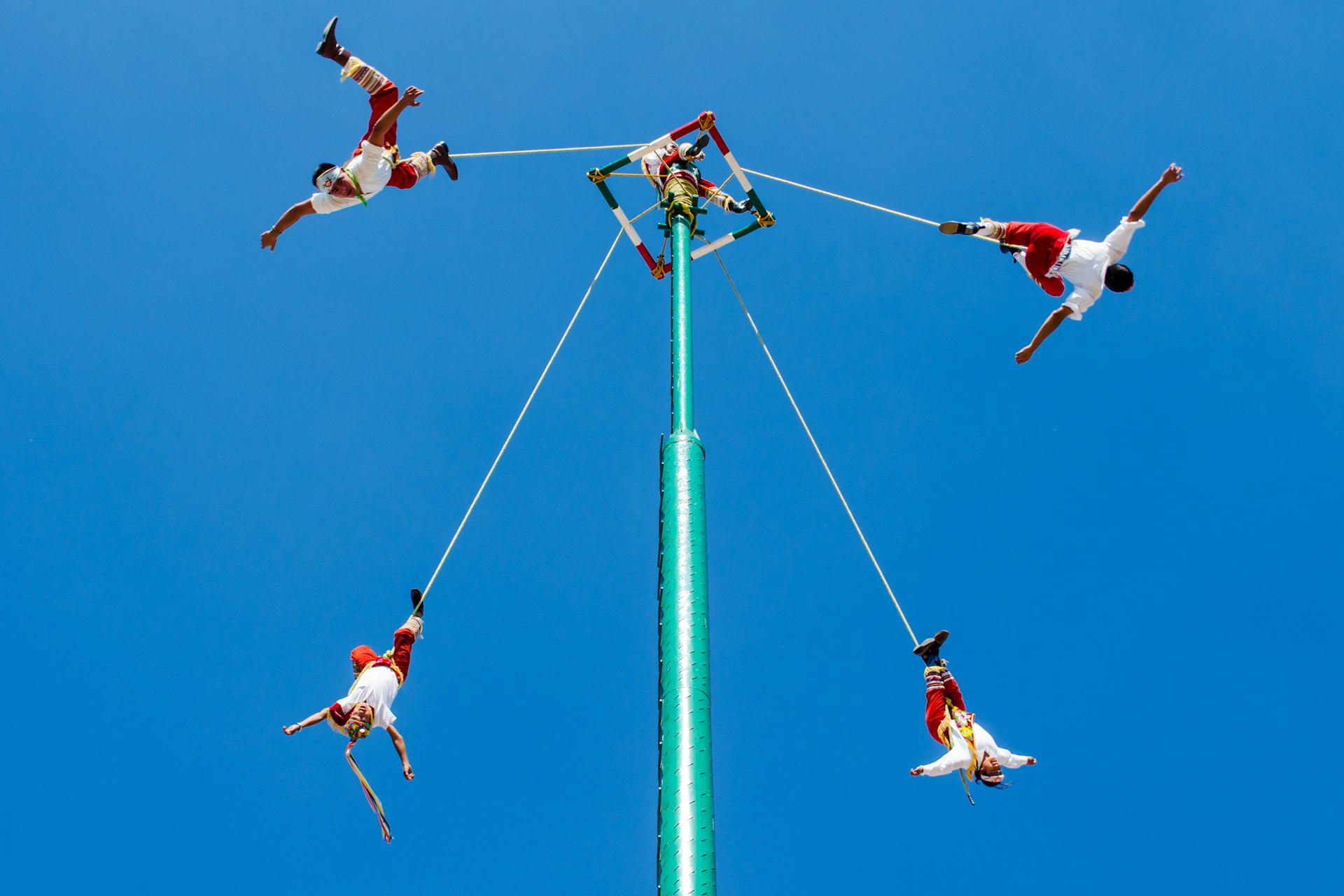 A group of men dressed in red suspended from a central pole - Voladores de Papantla