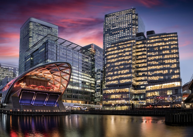 A business district with tall glass-and-steel buildings lit up at dusk