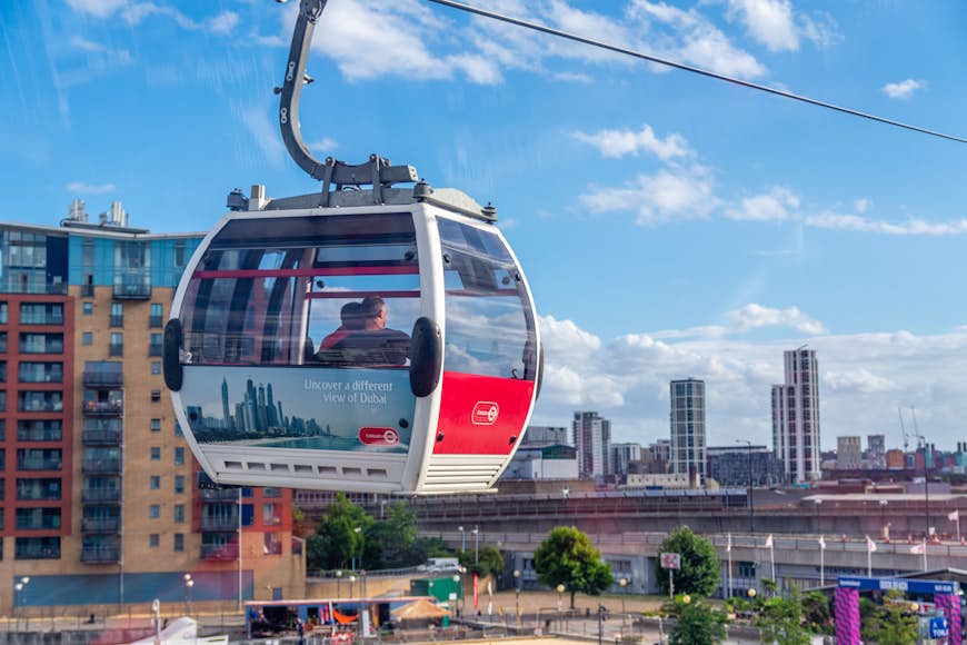 A cable car with two passengers travels through a developed area.