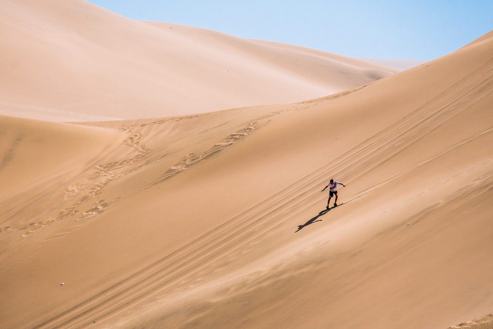 Silhouette of a man sandboarding in the desert of Peru.