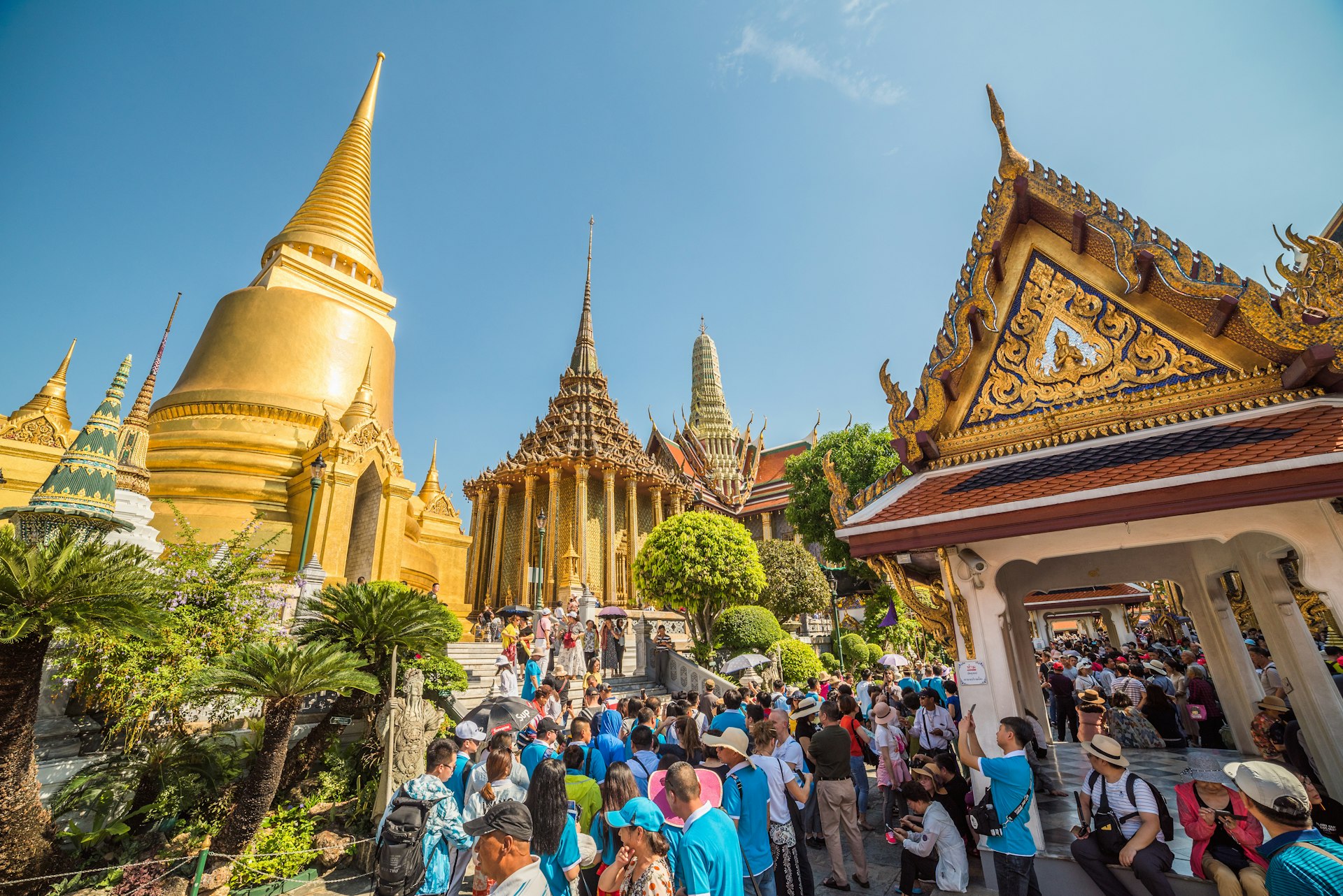 Many tourists gather in the Temple of Emerald Buddha at Bangkok's Grand Palace with a golden stupa in the left of the photo