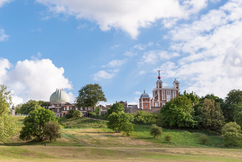 Royal Observatory in Greenwich Park A large expanse of green with a red-brick observatory building at the top of a hill