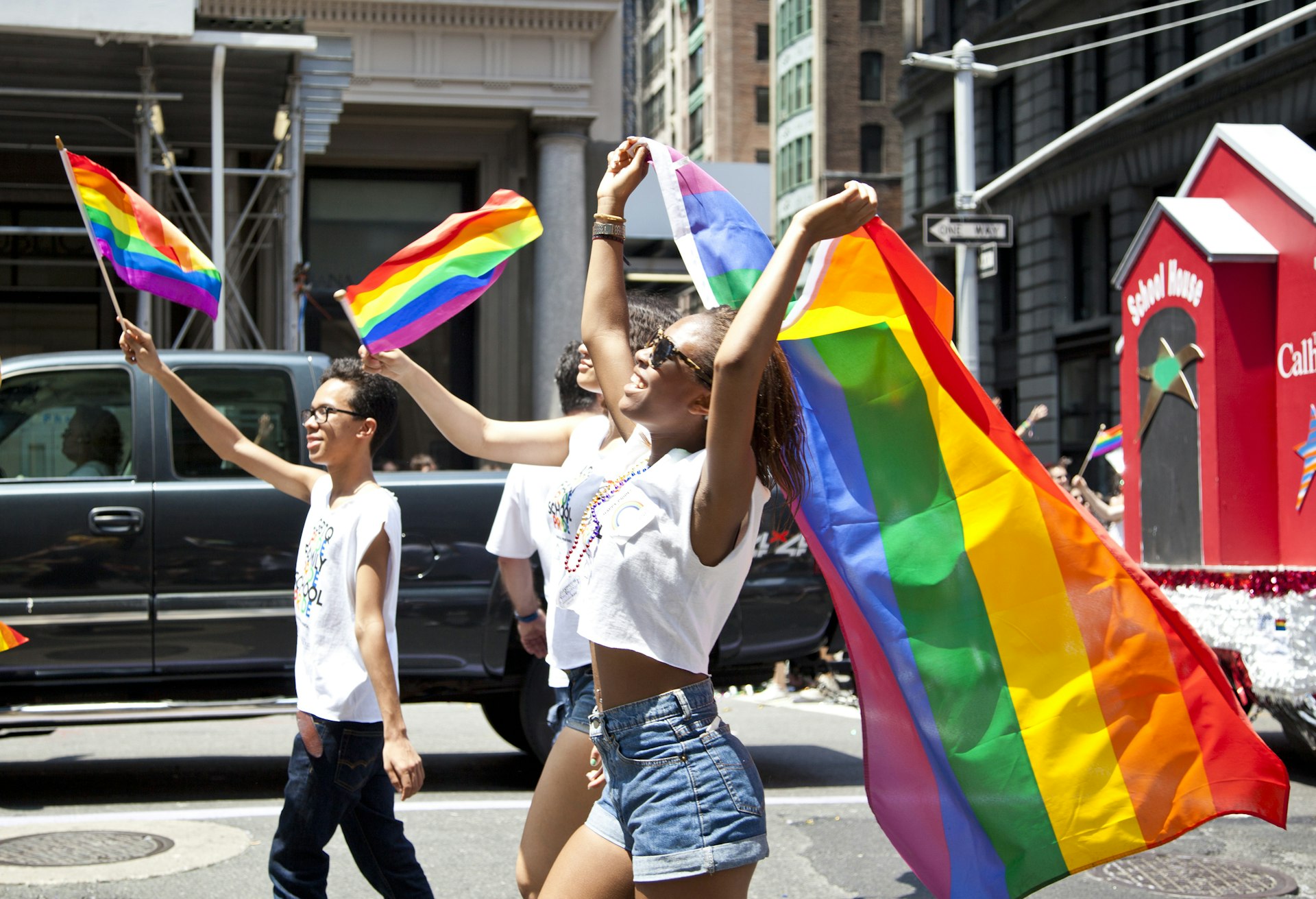 A group of people holding and flying rainbow flags walk down a street during NYC's Pride Parade.