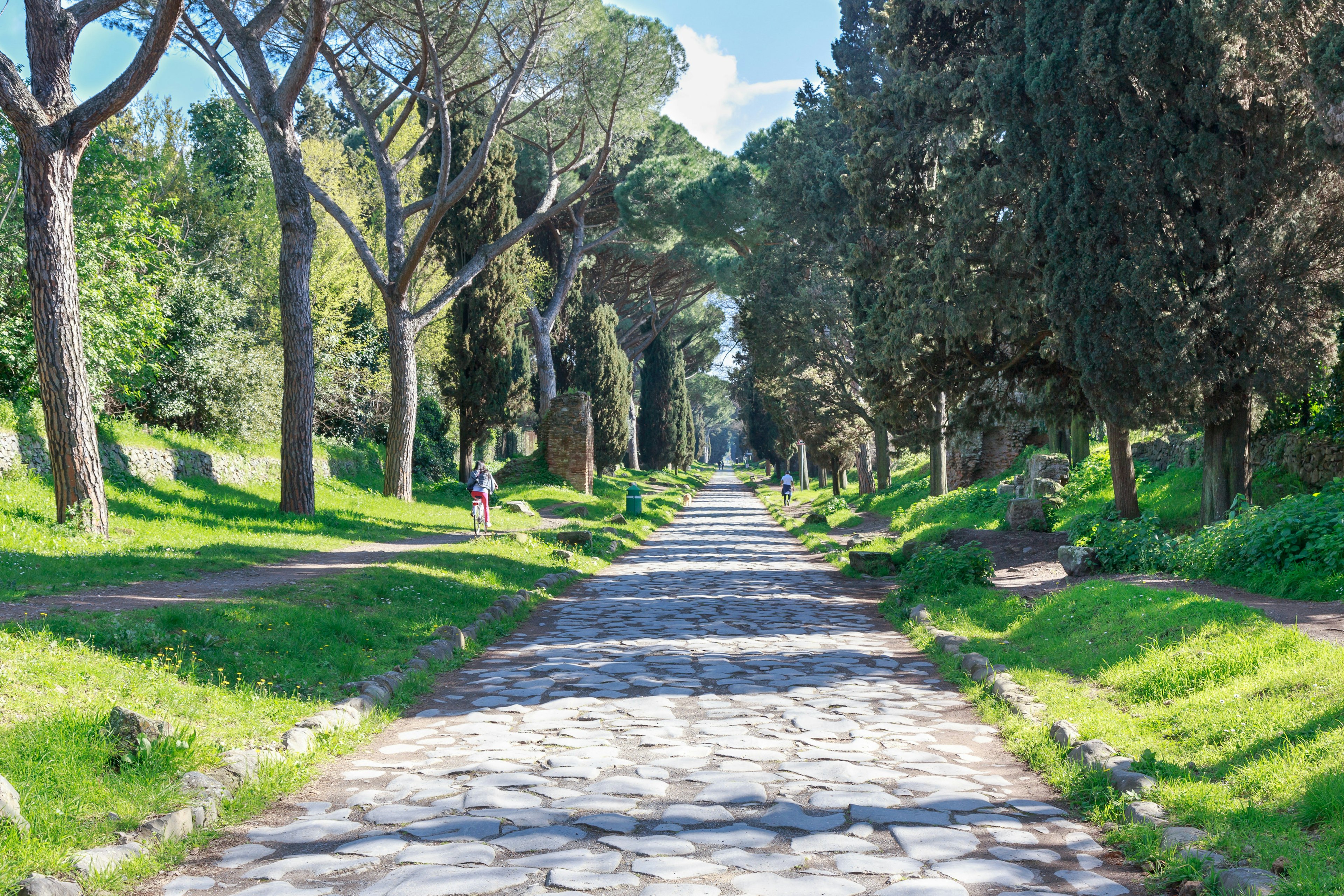 People riding bikes along the ancient tree-lined Via Appia Antica in Rome, Italy