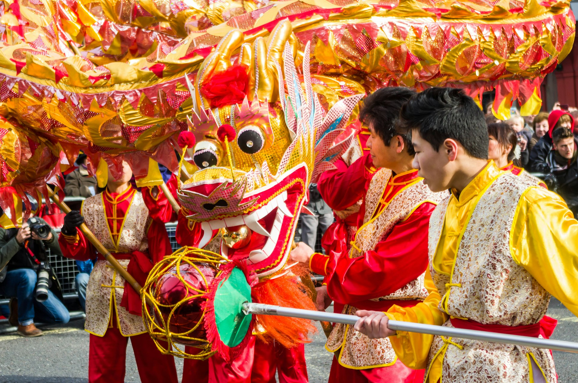 Золото-красный дракон на улицах в окружении людей, одетых в традиционную китайскую одежду.