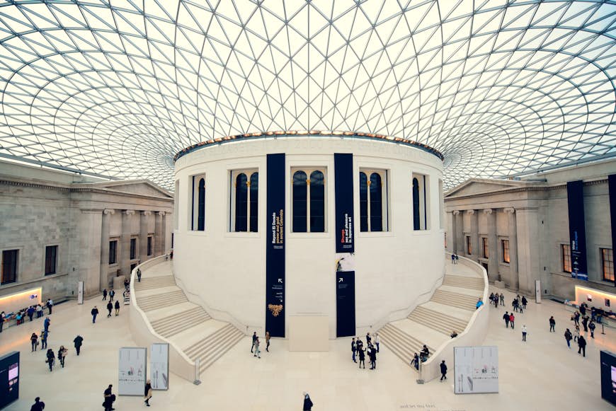 A large round atrium with a glass roof. People are milling around on the ground floor below