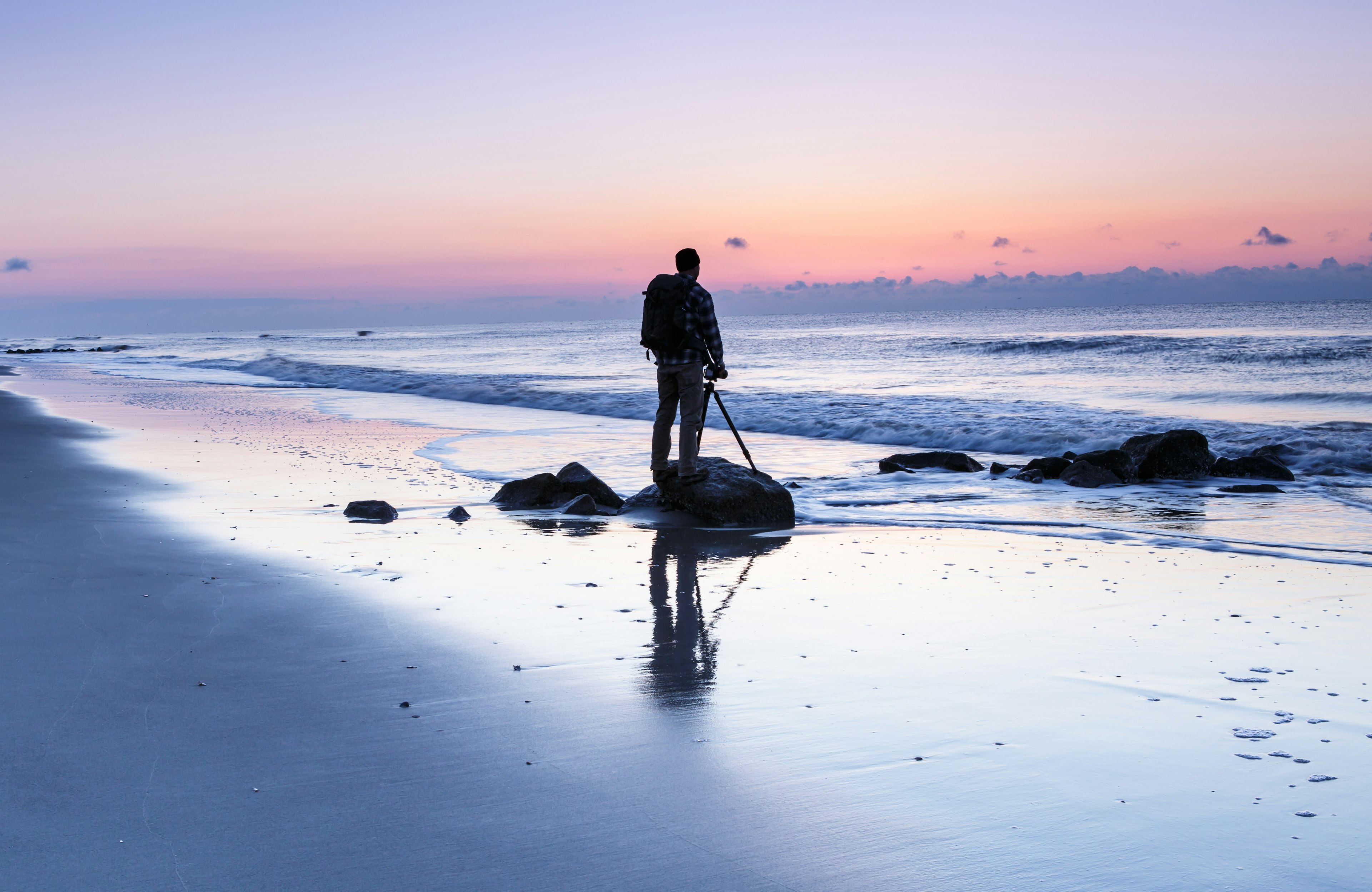 Silhouette of a solitary male photographer waiting for the sun to rise over the ocean at Folly Beach near Charleston.