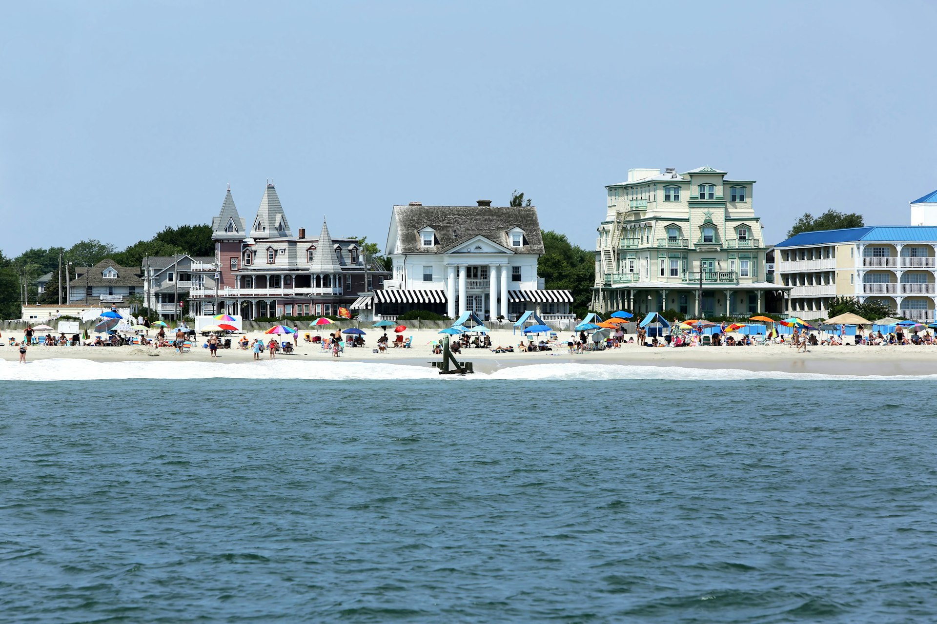 A shot of the shoreline taken from out at sea, showing Victorian buildings lining a beach filled with colorful umbrellas