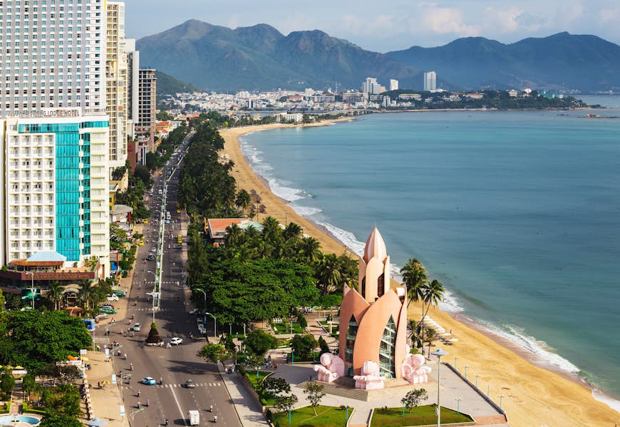 An aerial view of the beach of Nha Trang. The beach runs right alongside the city, with a number of skyscrapers and modern buildings visible just behind the golden sands.