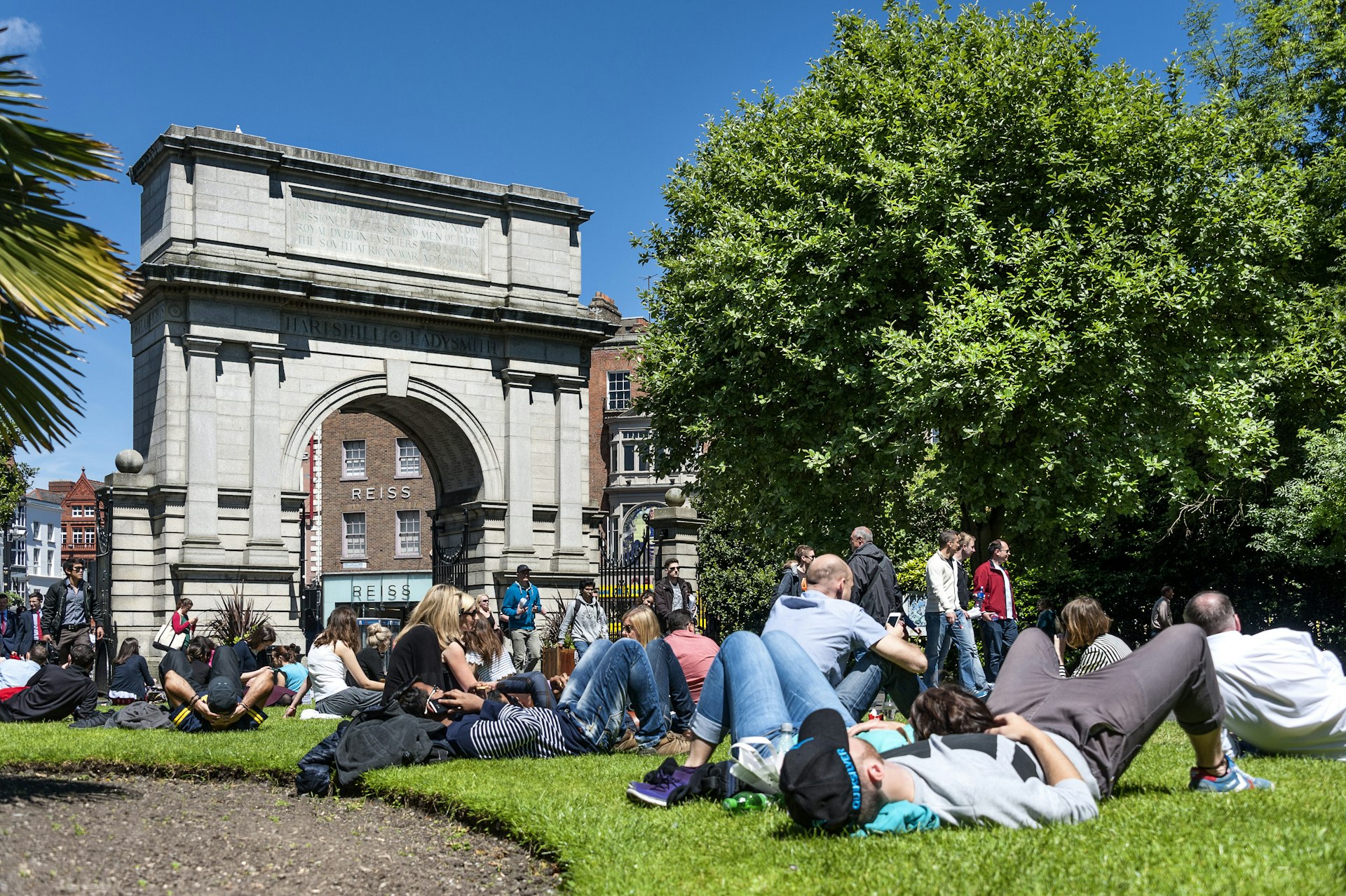 People rest on the grass next to Fusilier's Arch on a sunny day in St Stephen's Green in Dublin