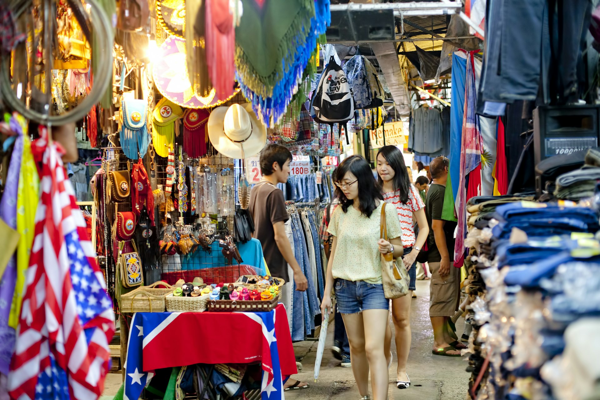 Tourists check out the hanging bags and hats at the stalls of Chatuchak Weekend Market in Bangkok, Thailand.