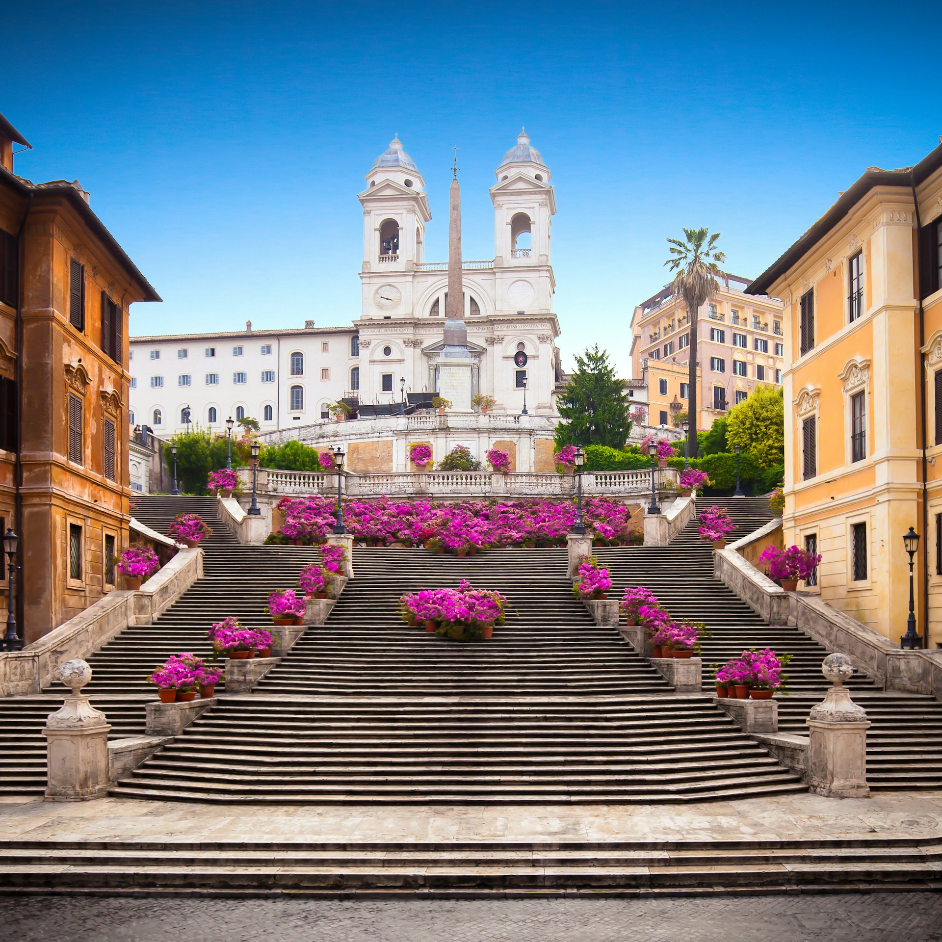 A wide staircase leads to a white church. Pink flowers line the steps