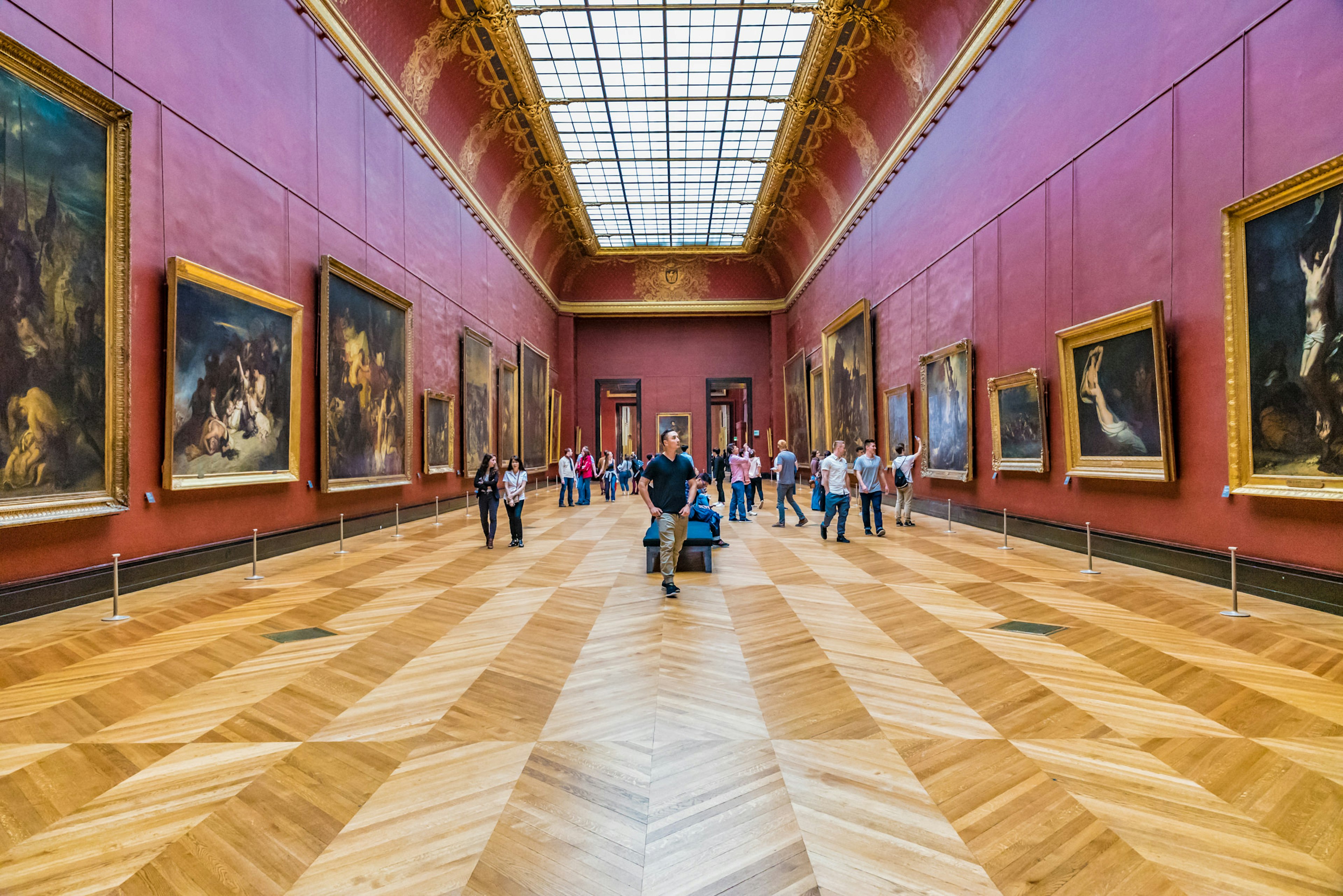 People stoll through a large hall in the Louvre, looking at art.