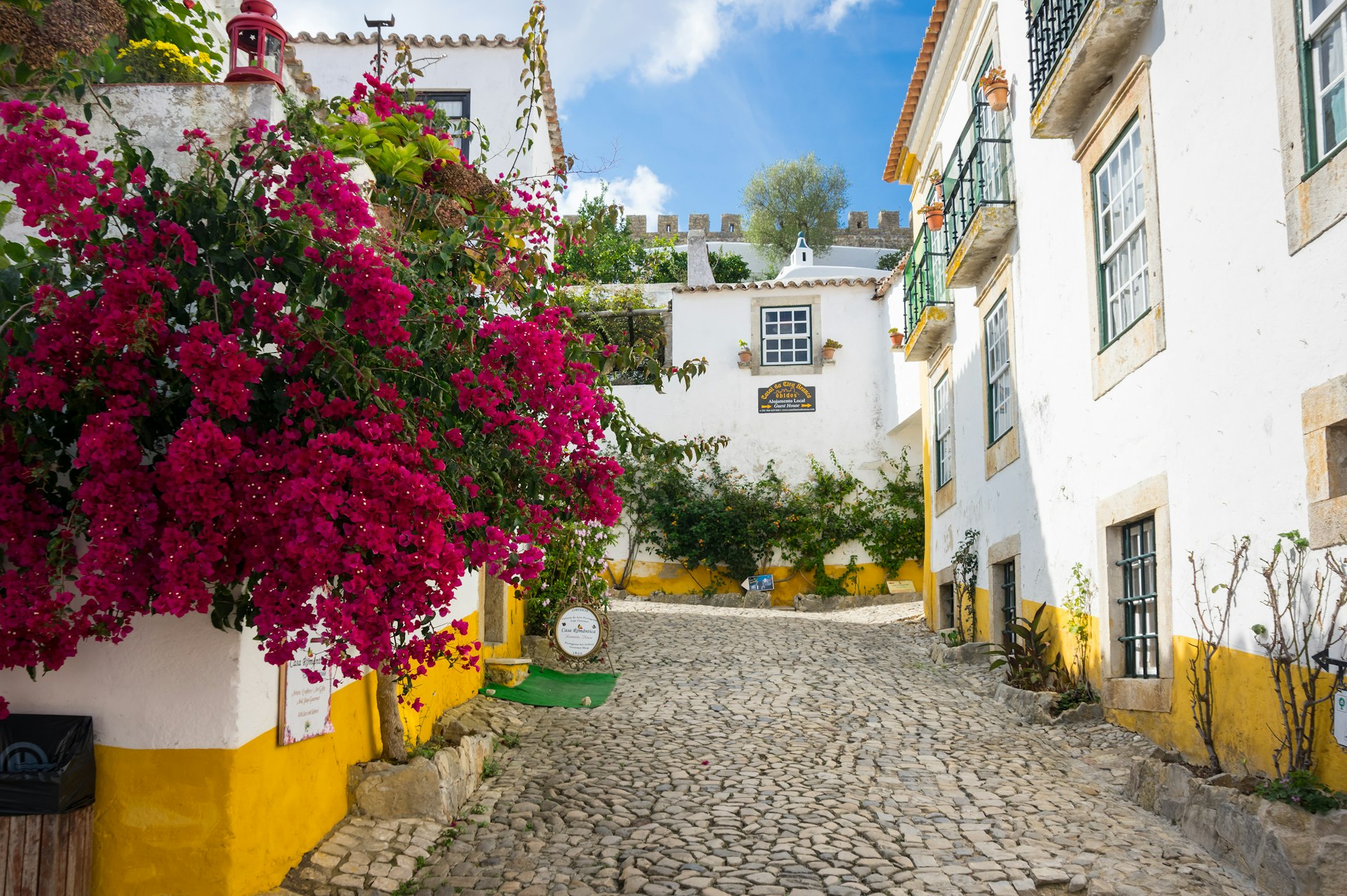 White-washed buildings with yellow trim are lined with bougainvillea in a Portuguese town. 