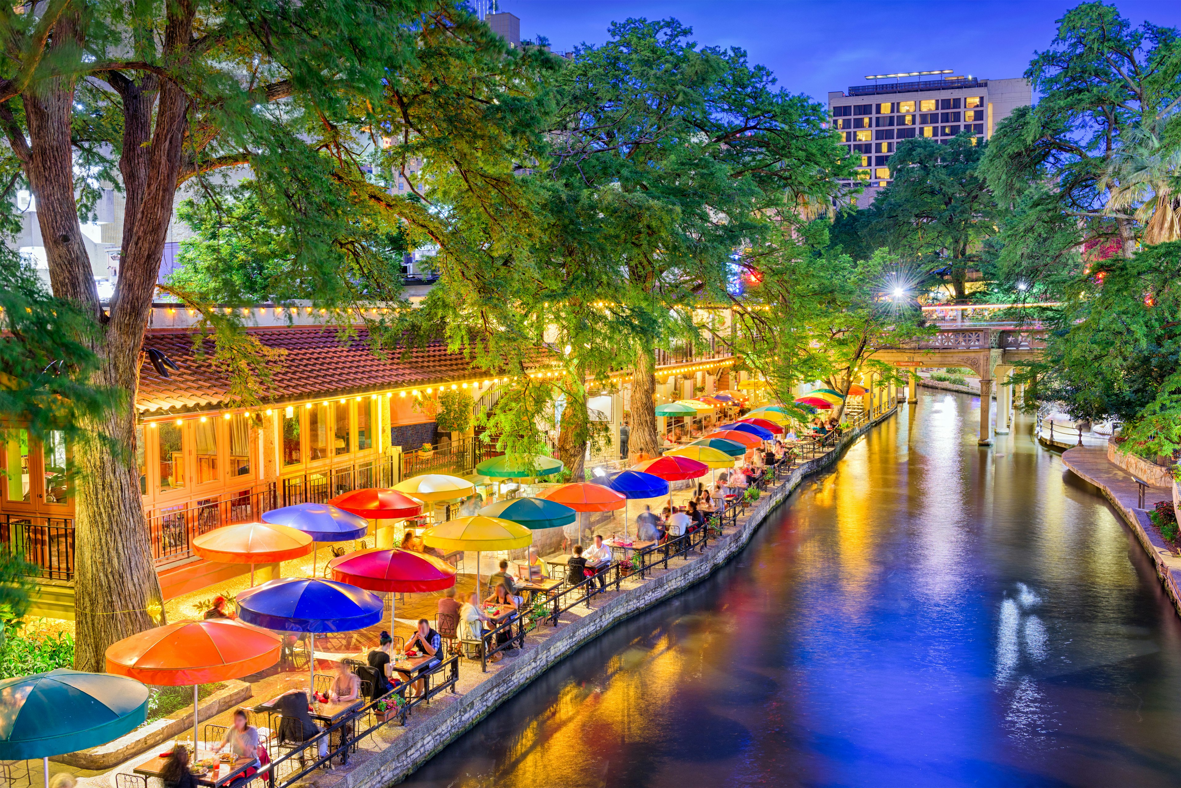 A river runs through a city, with an embankment lined with restaurants and colorful umbrellas