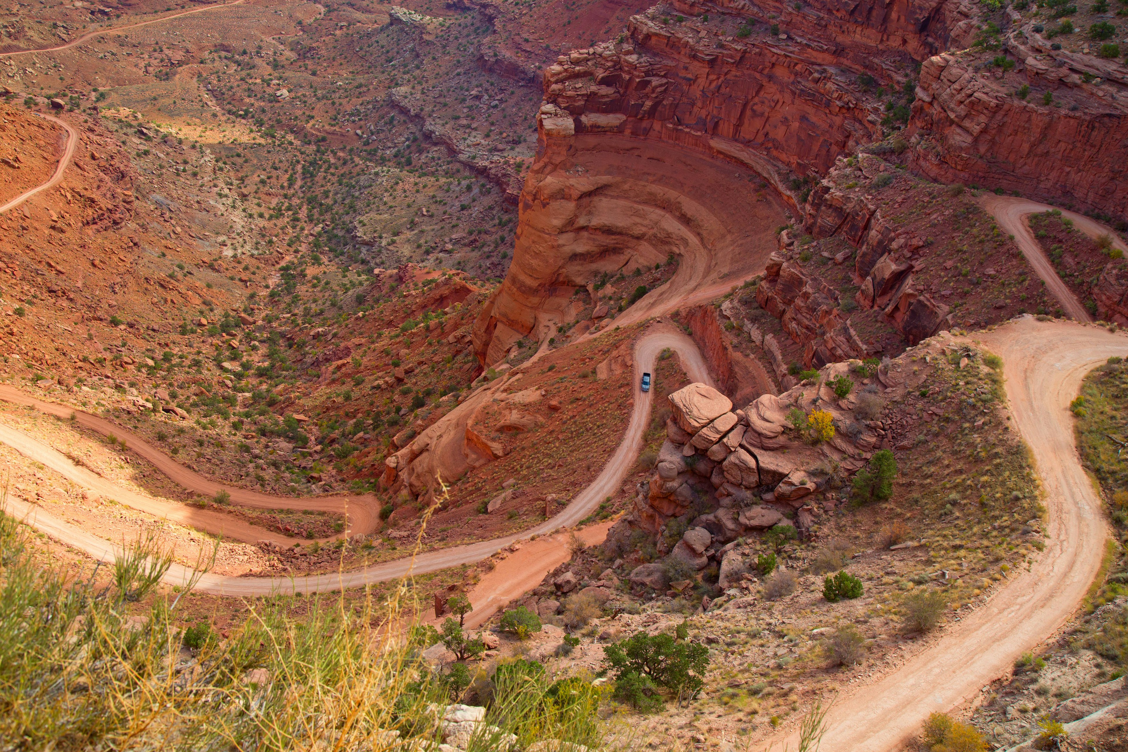 A birdseye view of a car driving up a windy dirt road