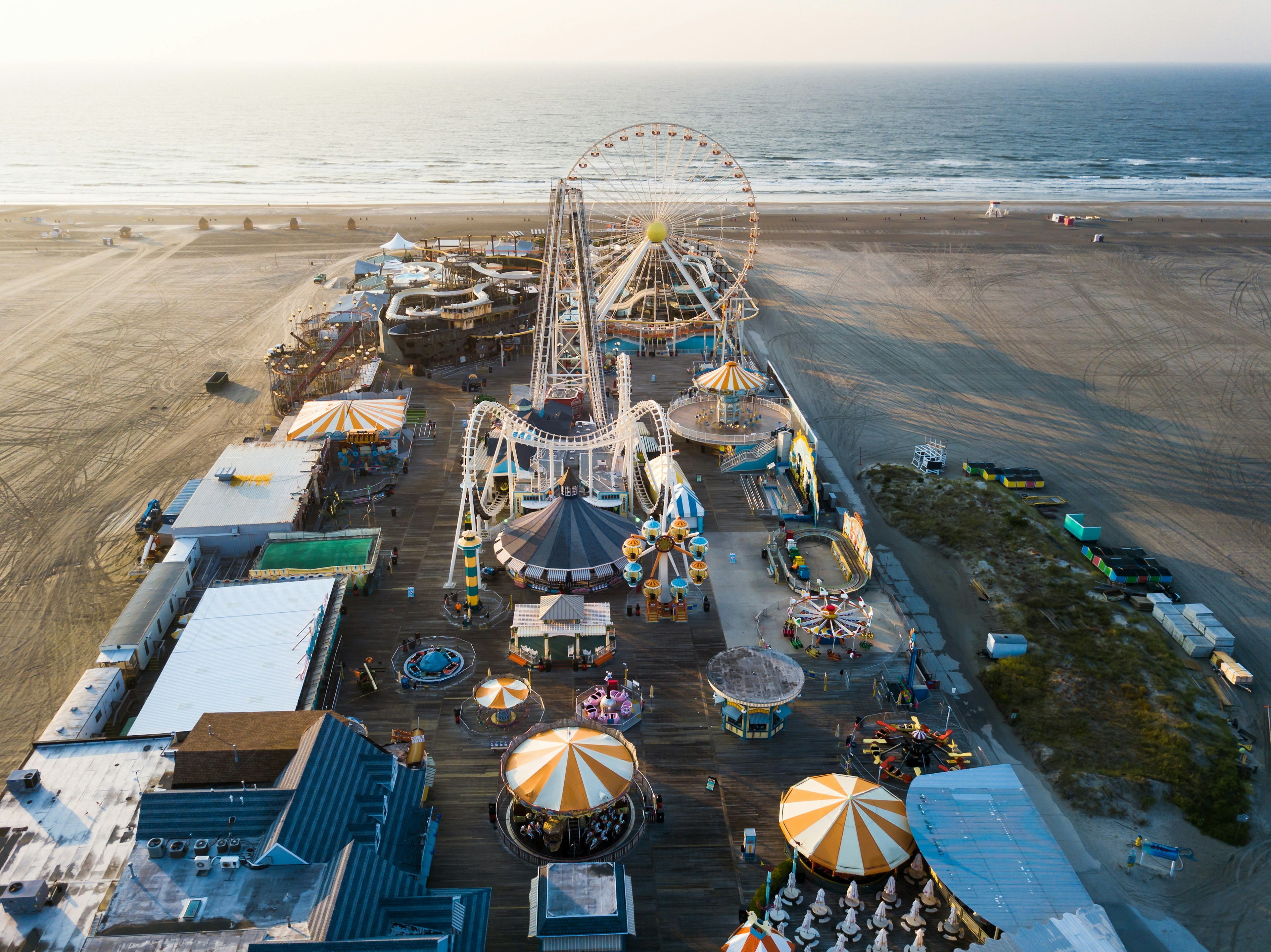 An aerial shot of a pier lined with amusements and rides, including a huge Ferris Wheel, carousel, and rollercoaster