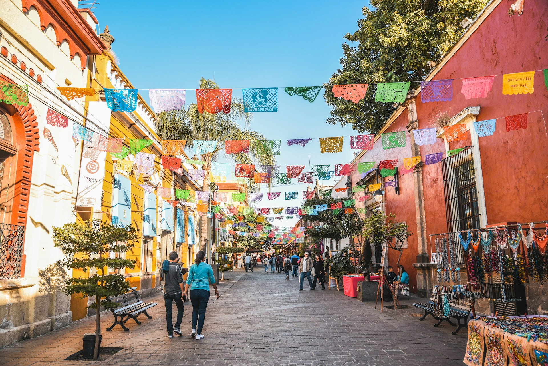 People walk down a stall-lined pedestrianized street with colorful bunting hanging overhead 