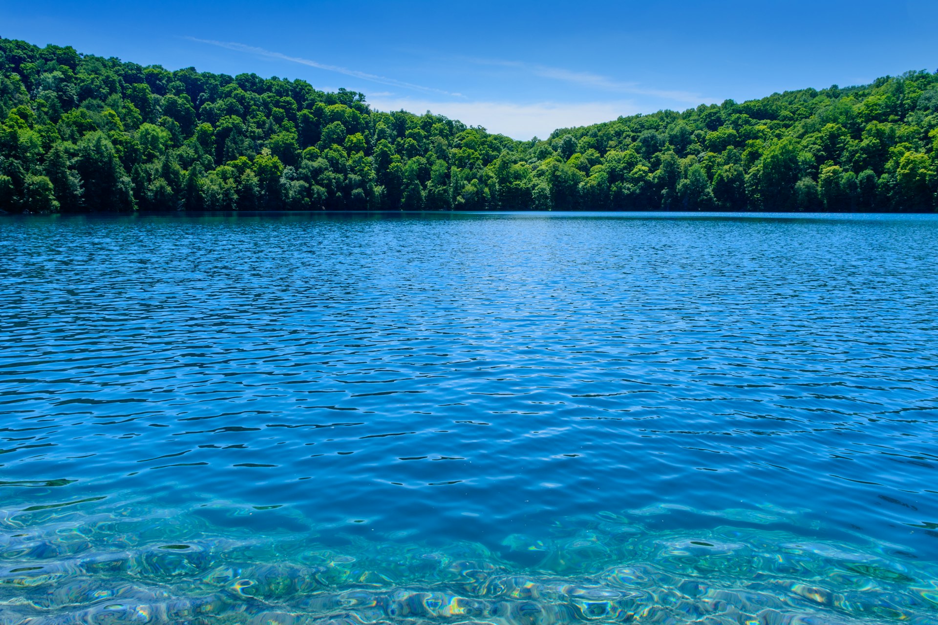 Blue waters over a rocky shore with trees in the background on a sunny day at Green Lakes State Park, New York State