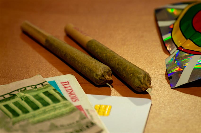 Recreational cannabis legalization in Illinois. Two marijuana joints are displayed with an Illinois ID card and money on a table.