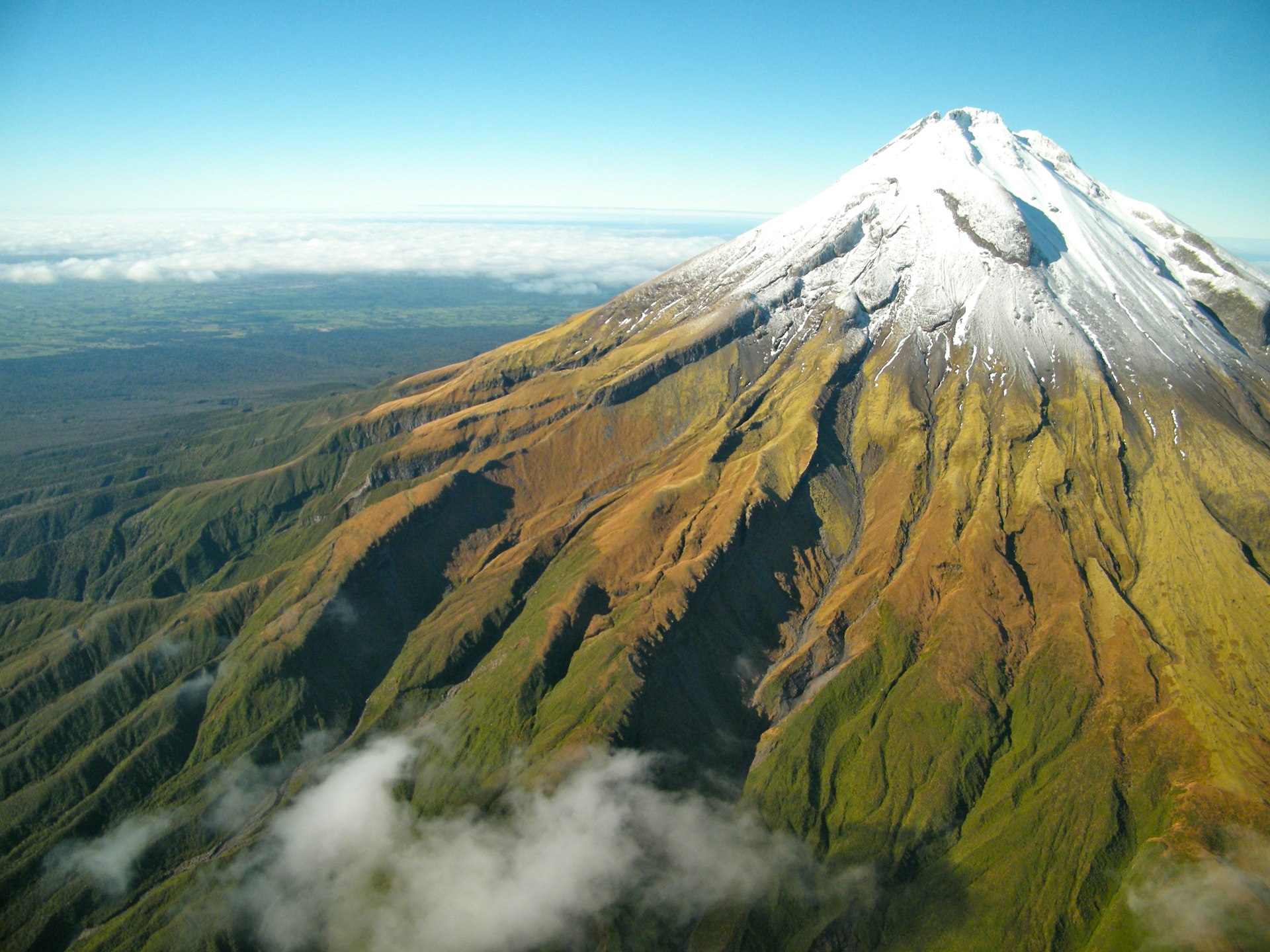 Green bush leads up to a snow-capped top of Mt. Taranaki in Egmont in New Zealand 