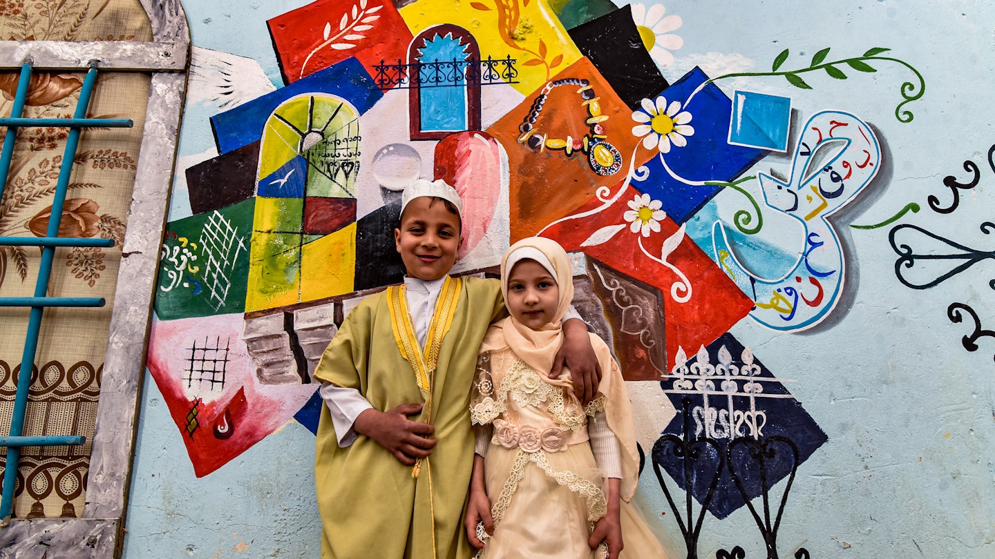 Children pose for a photo in front of a large graffiti depicting cultural elements including mosques, churches, old window lattices of the old town of Iraq's northern city of Mosul, on the first night of the Muslim holy fasting month of Ramadan on April 13, 2021, during a celebration hosted by a local cultural NGO. (Photo by Zaid AL-OBEIDI / AFP) (Photo by ZAID AL-OBEIDI/AFP via Getty Images)