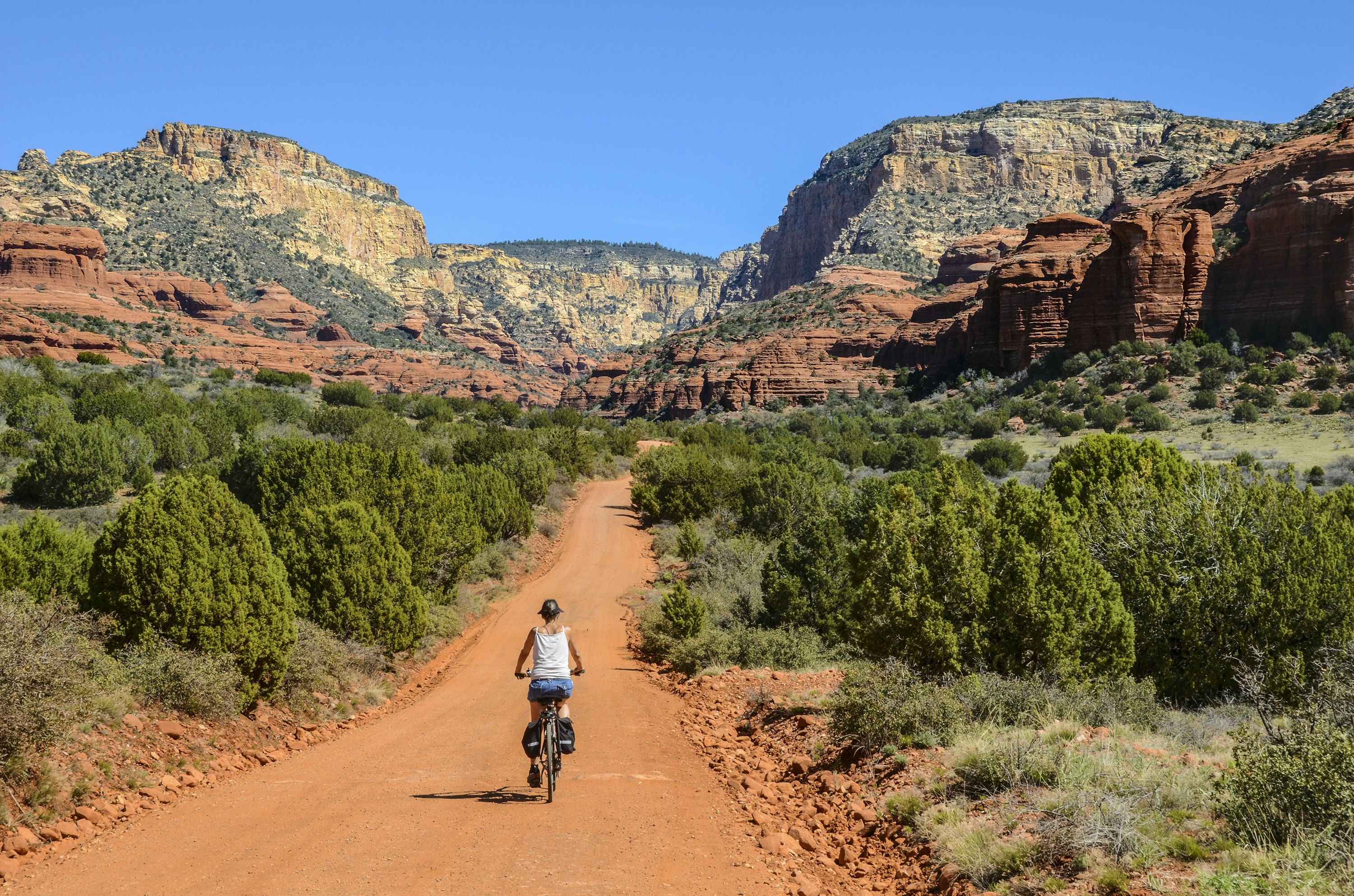 A person is riding their bike down a dirt path surrounded by red rocky peaks